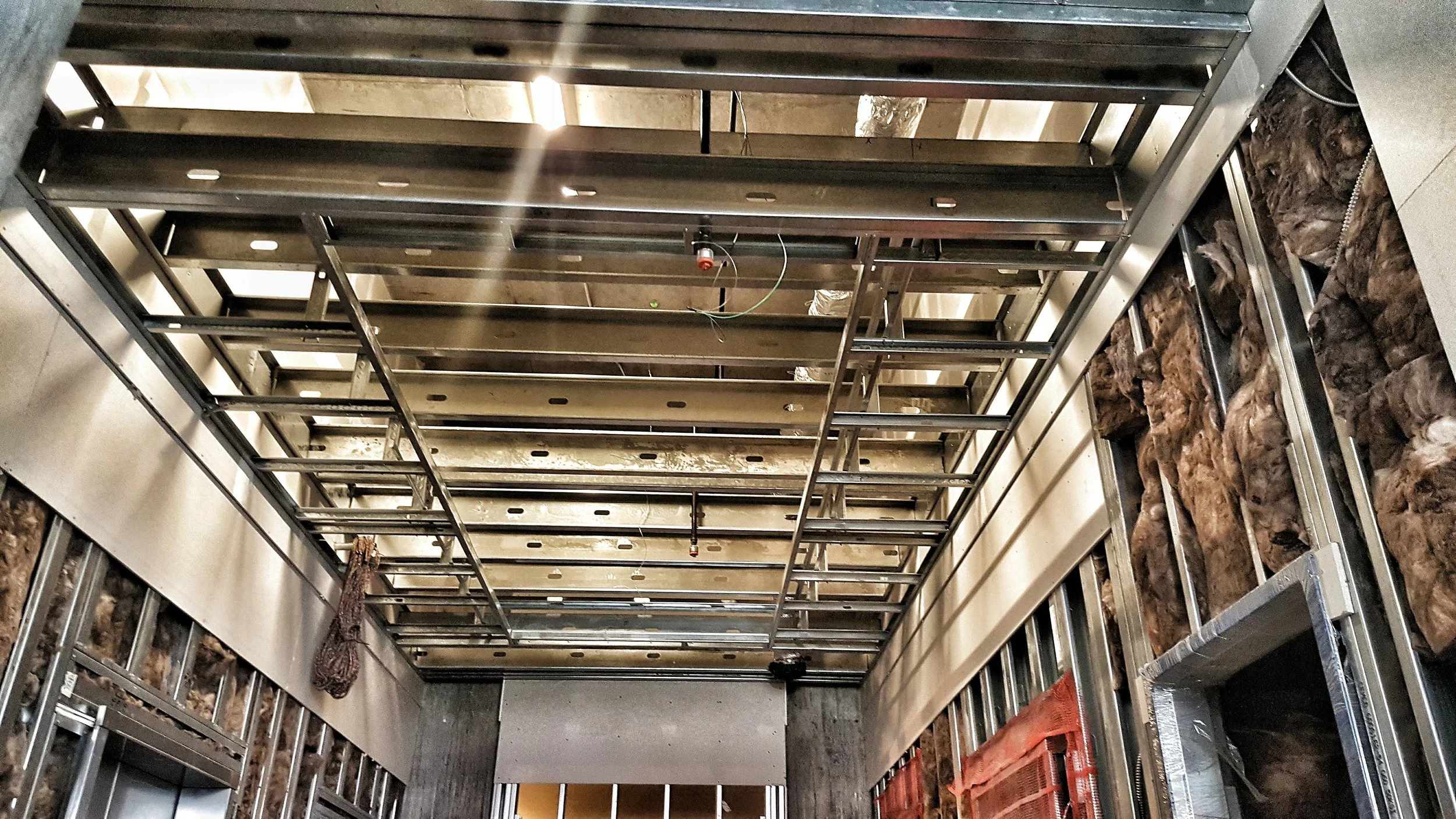 Construction of a building interior with metal framing, exposed insulation, and partially installed drywall.