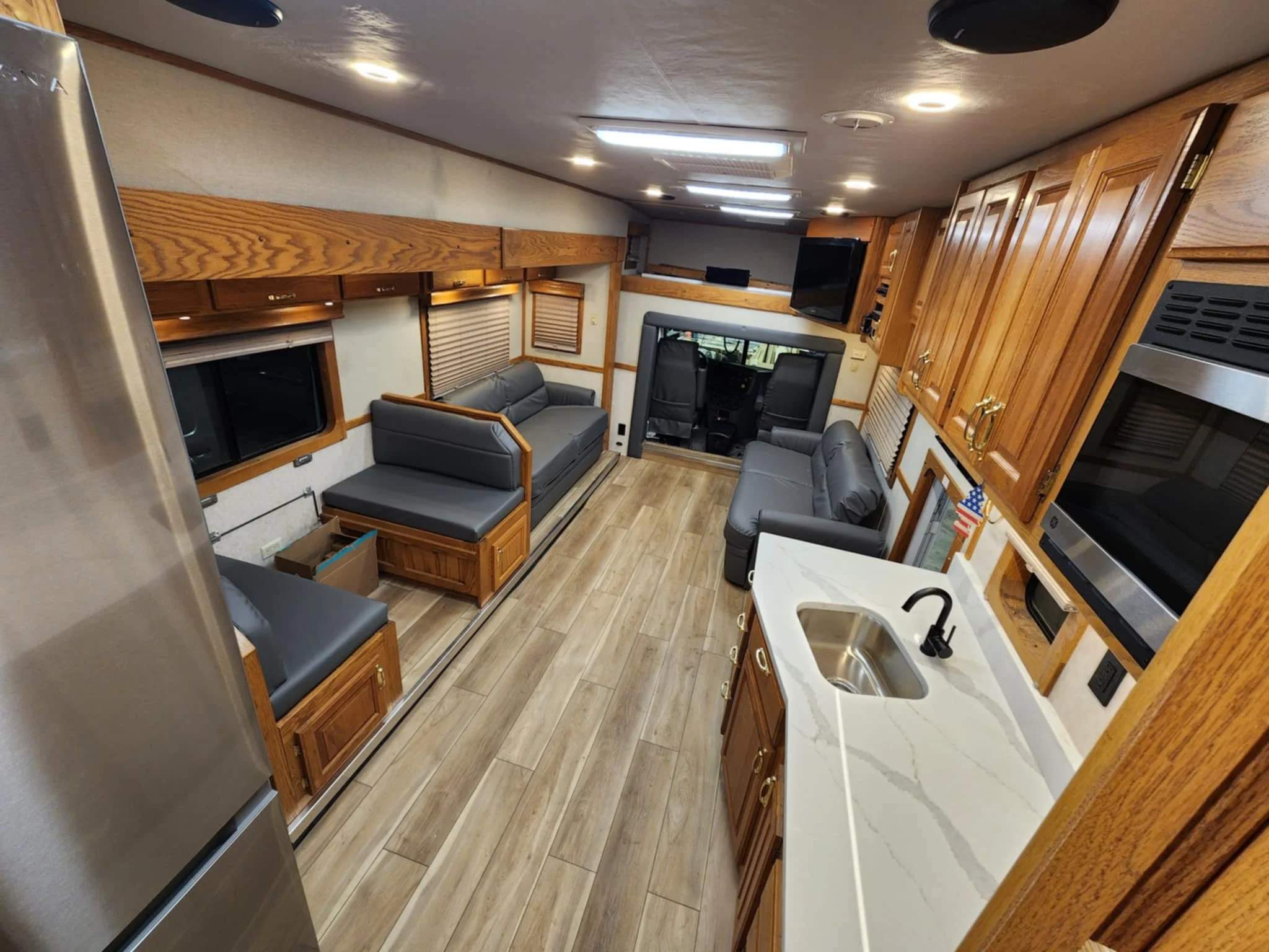 Motor home Interior of a recreational vehicle with wood cabinets, gray sofas, a kitchen sink, and a mounted TV.