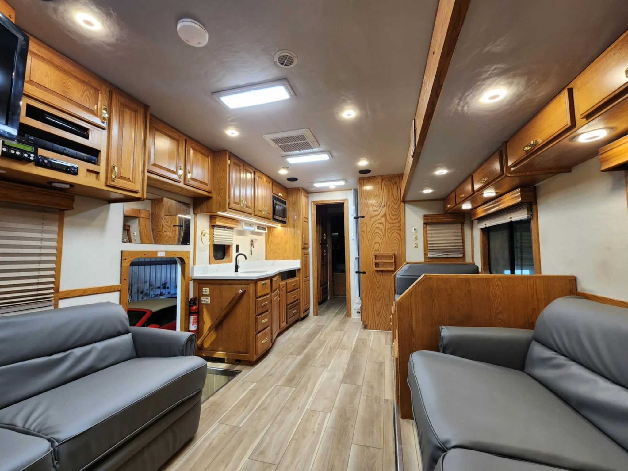 Motorhome Interior of a living area with wooden cabinetry, gray sofas, a kitchen with a white counter, and windows with blinds.