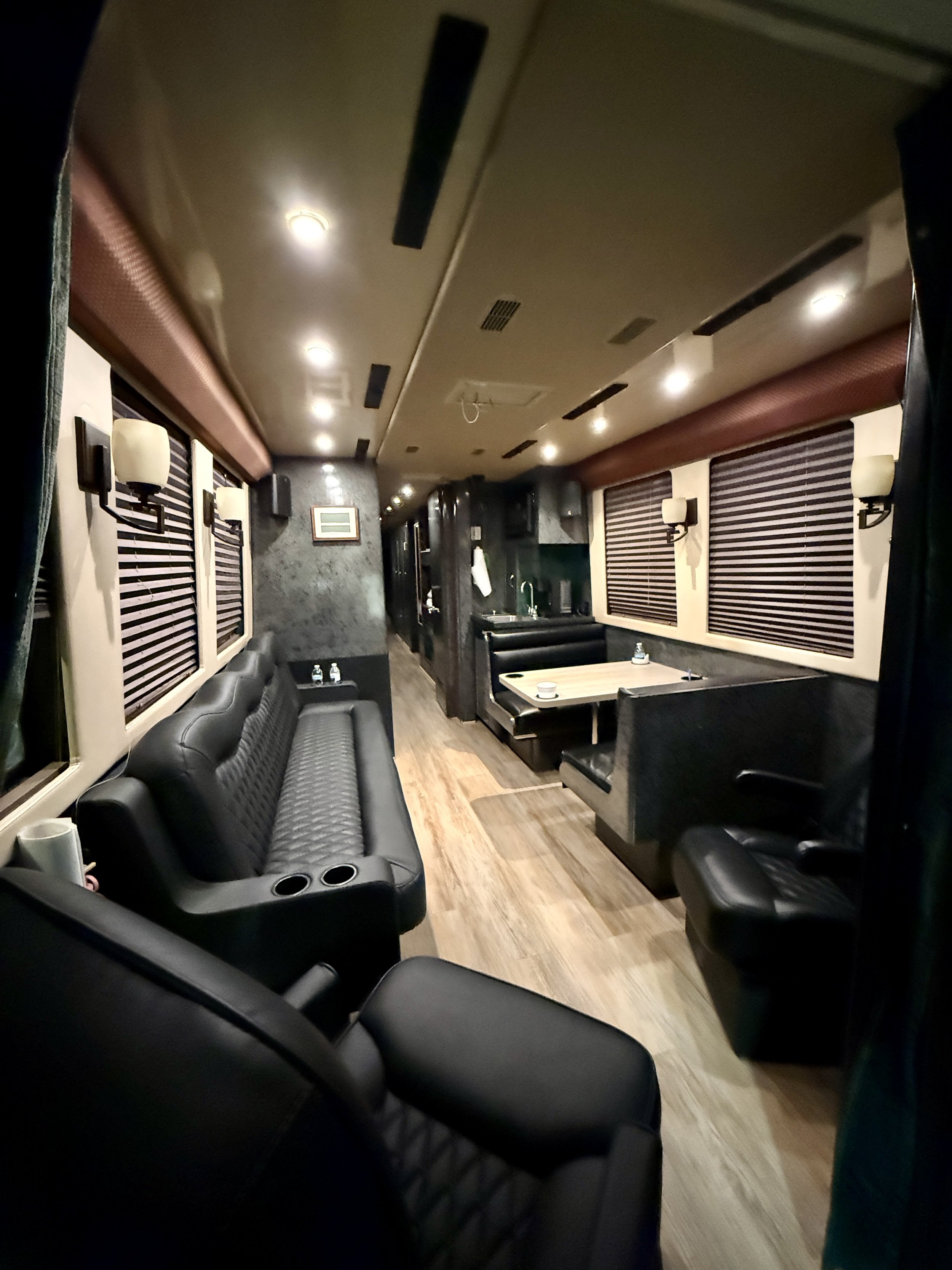 Tour bus Interior of a small lounge or VIP area with black leather seating, wooden flooring, and window blinds.