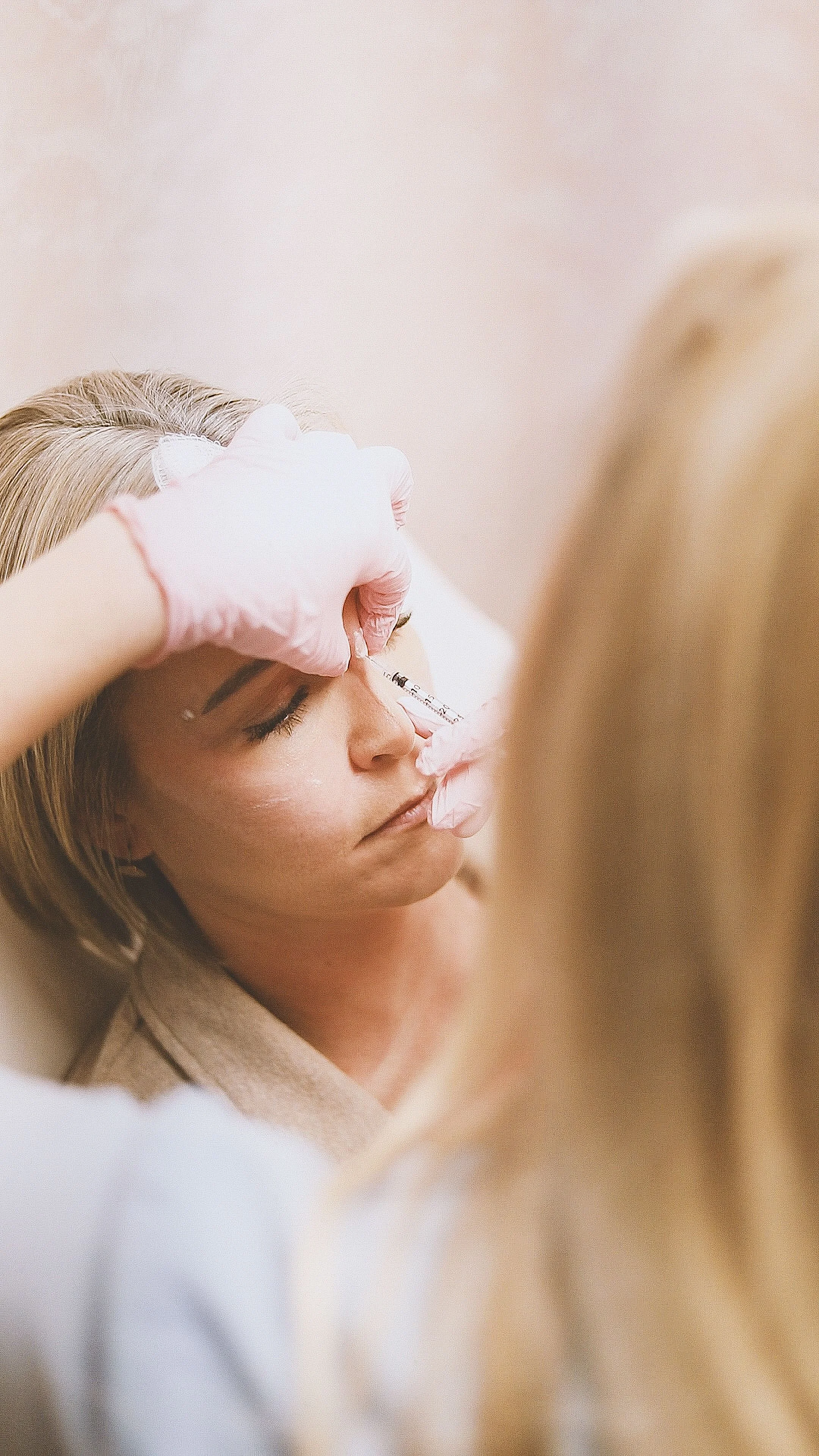 A woman receiving a cosmetic treatment or injection in her face, administered by a professional wearing pink gloves.
