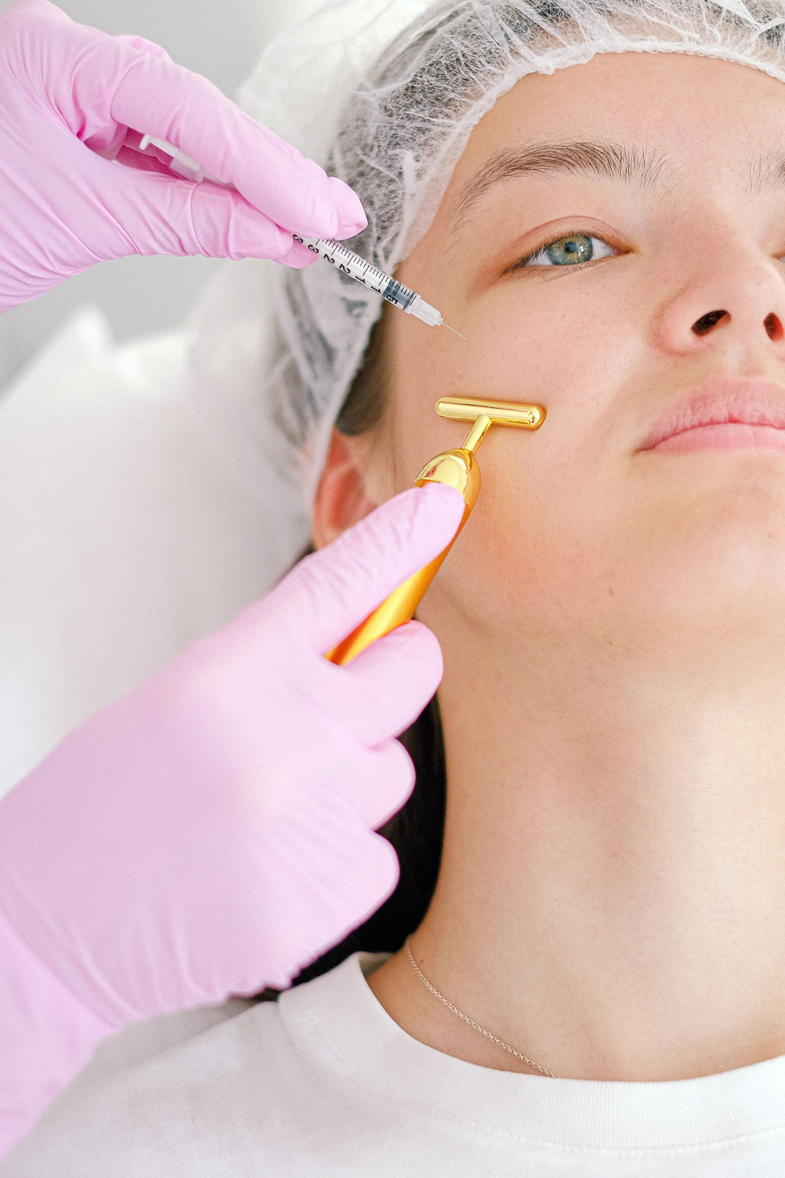 Medical professional in pink gloves injecting filler into woman's cheek with a syringe.