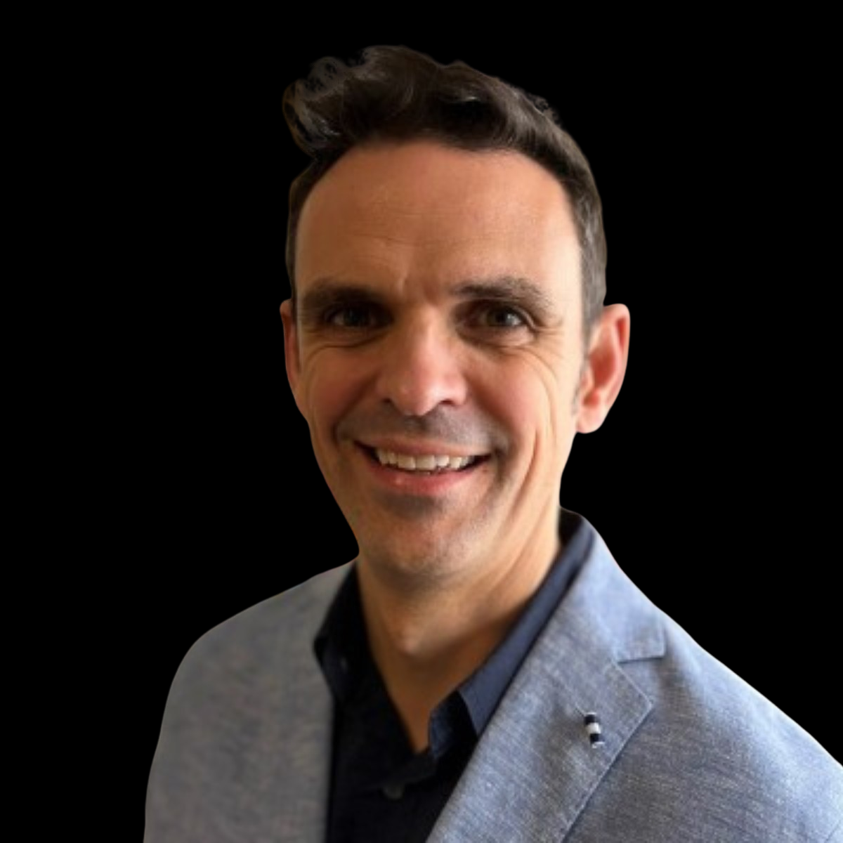 Portrait of a smiling man with dark hair, wearing a light gray blazer and a dark shirt against a black background.