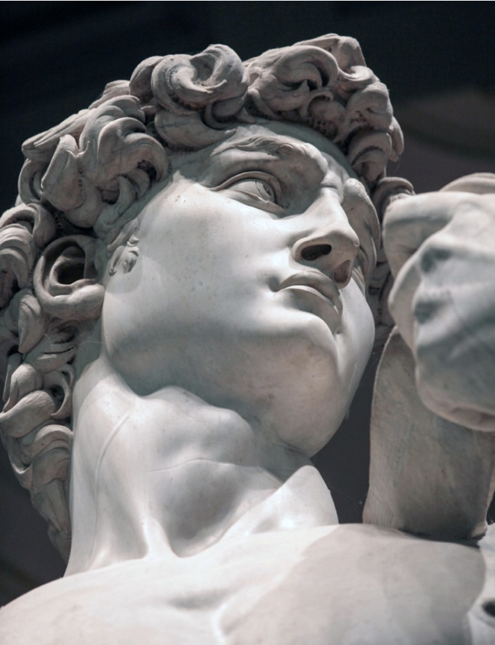 Close-up of the marble statue of a man's head with curly hair, looking upward.