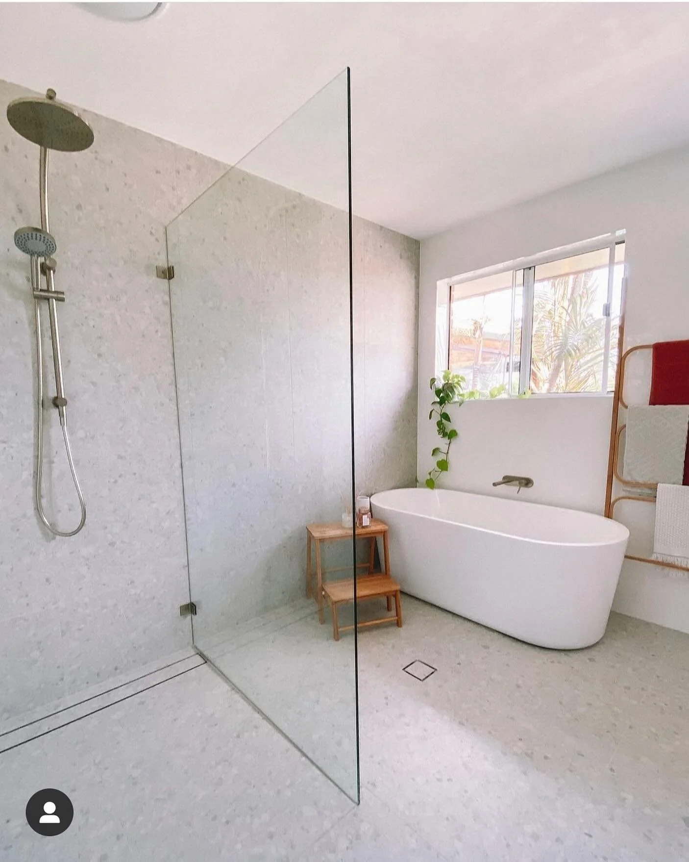 Modern bathroom with walk-in shower, freestanding bathtub, wooden stool, towel rack, and large window with a view of trees.