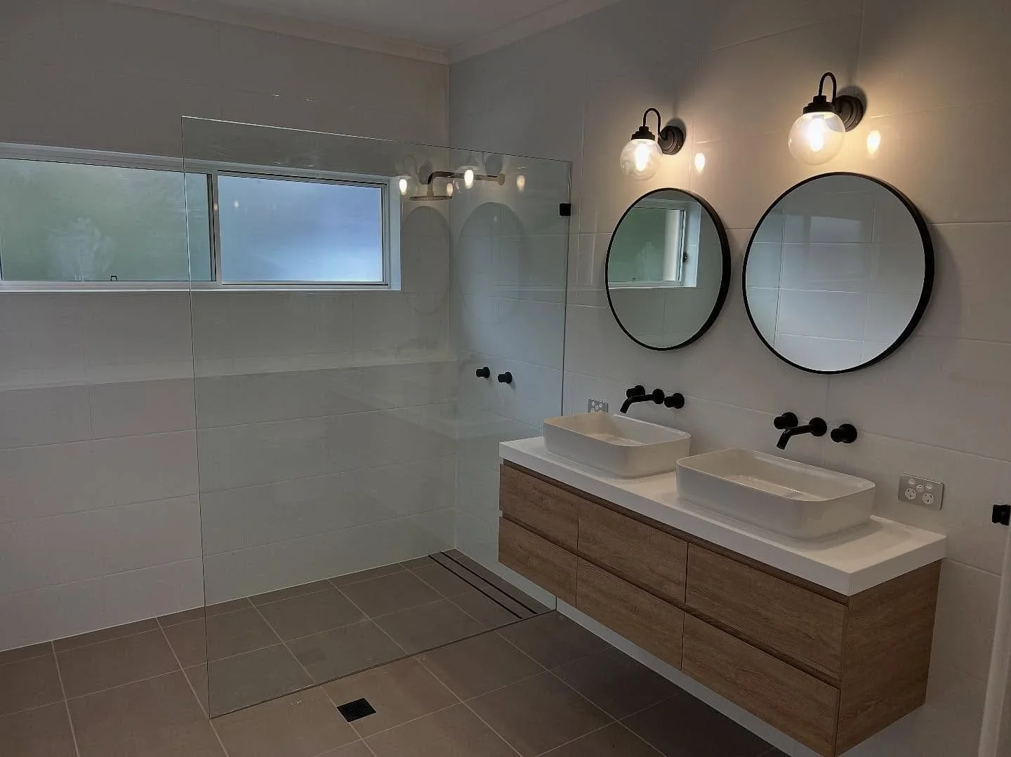 Modern bathroom with double vanity, vessel sinks, round mirrors, and wall-mounted light fixtures.