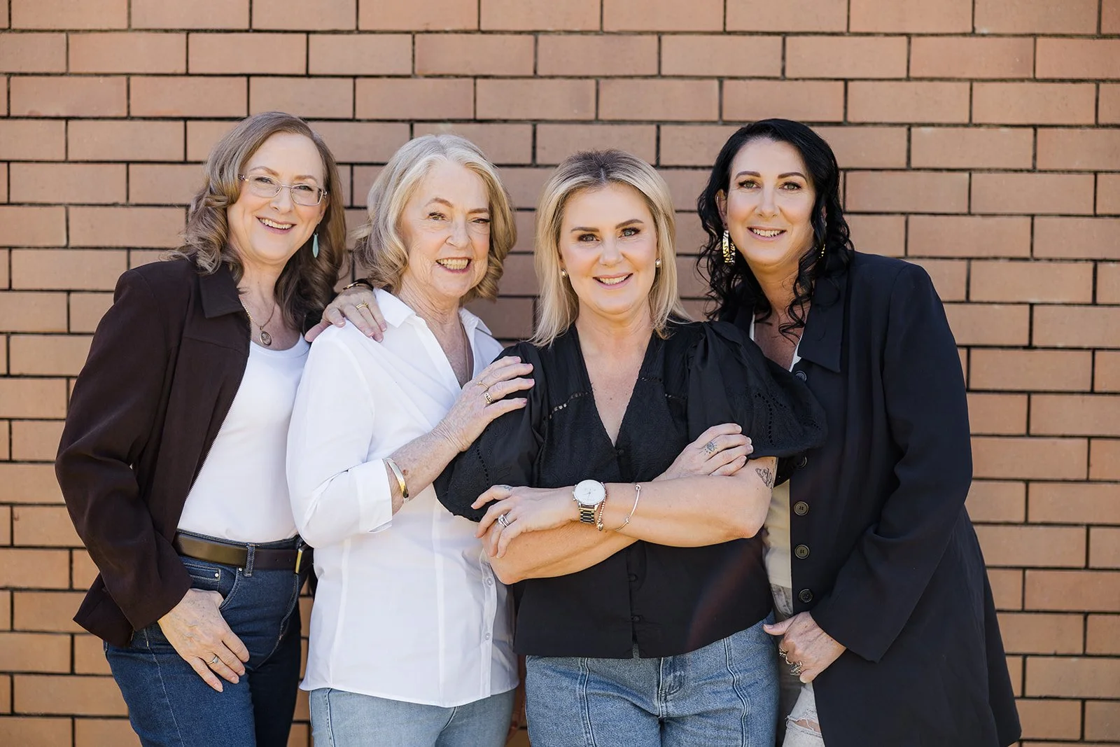 Four women standing in front of a brick wall smiling and posing for the camera.