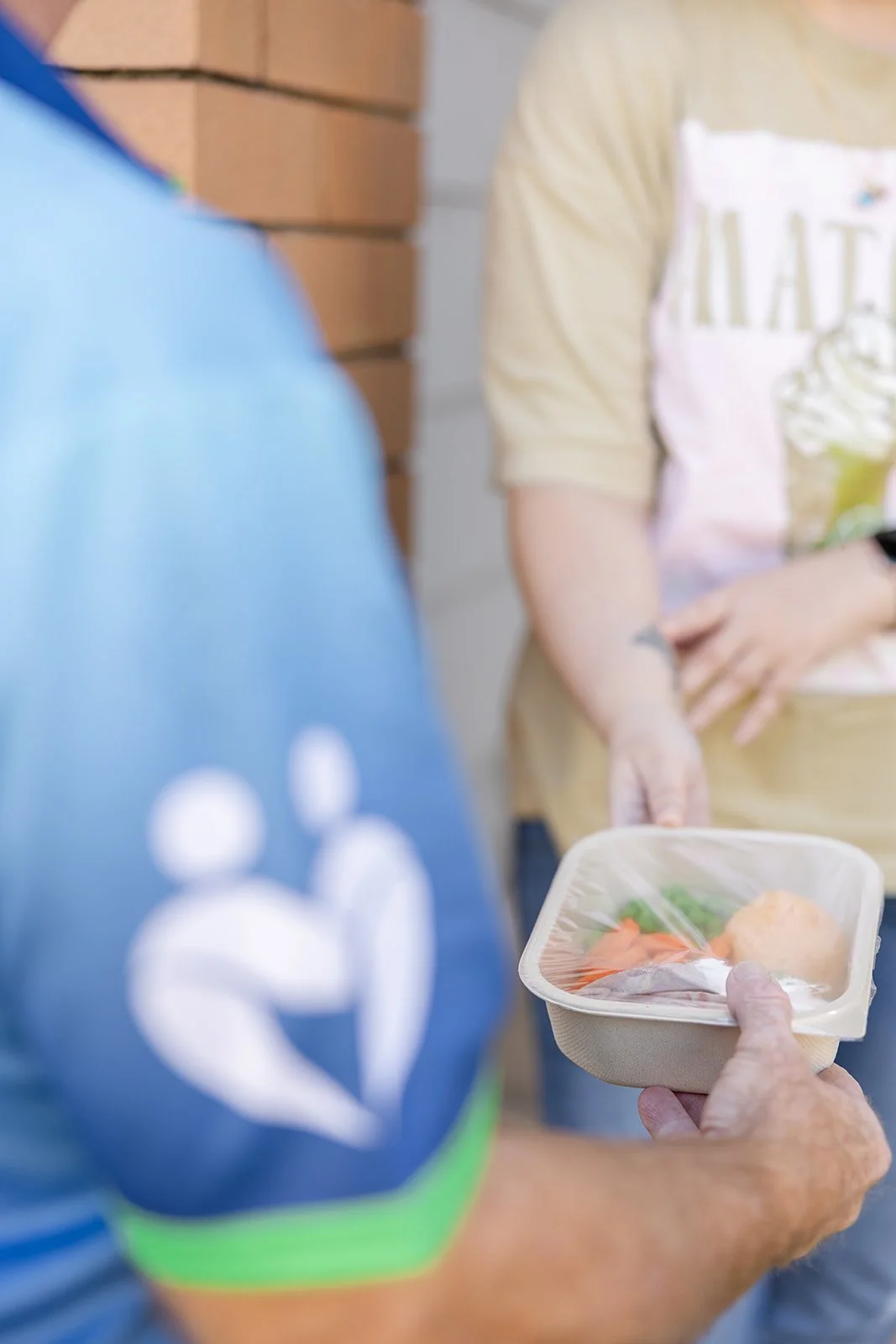 Person holding a food container with vegetables receiving it from another person wearing an apron.