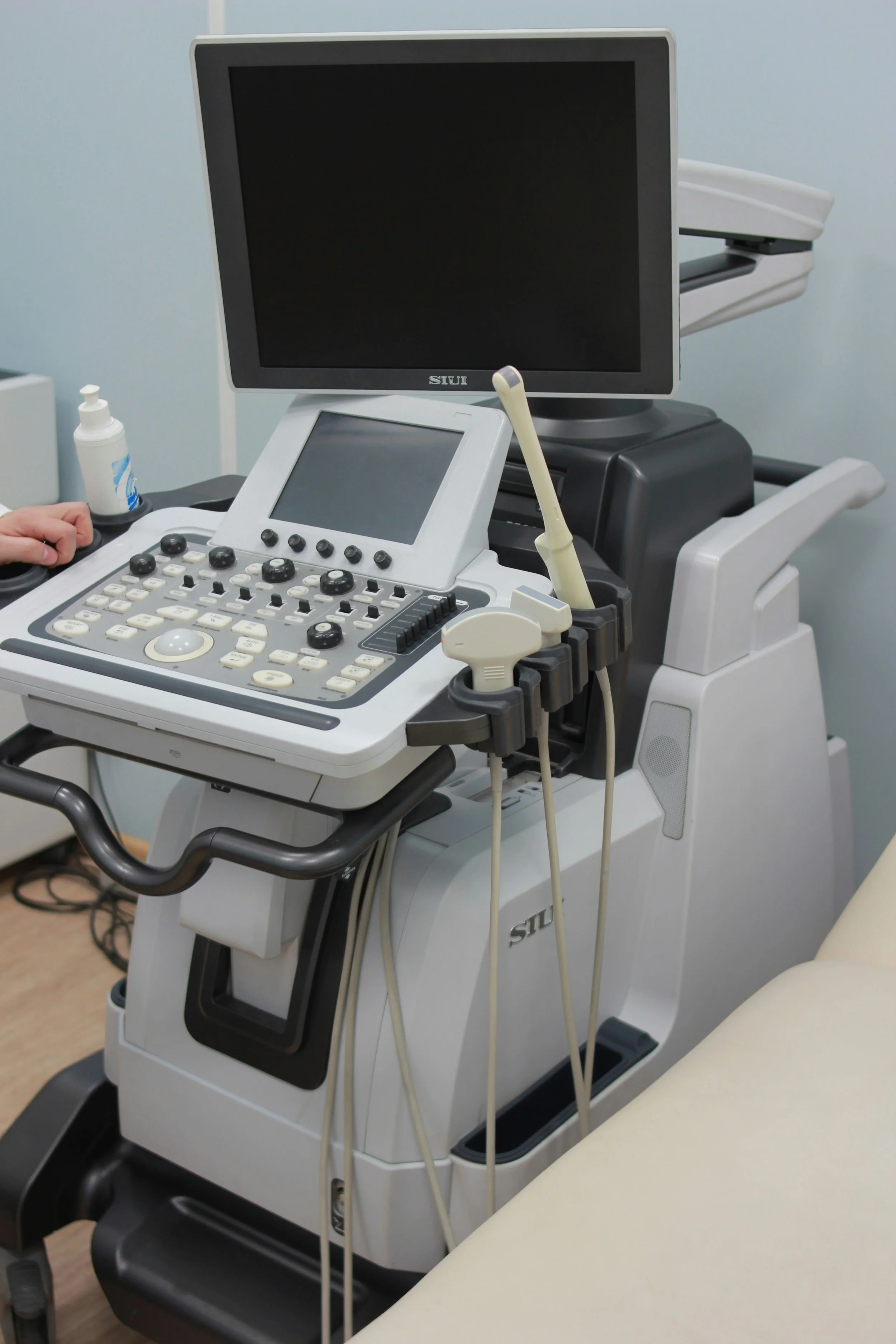 Medical ultrasound machine with monitor, control panel, and ultrasound probes in a clinical setting.