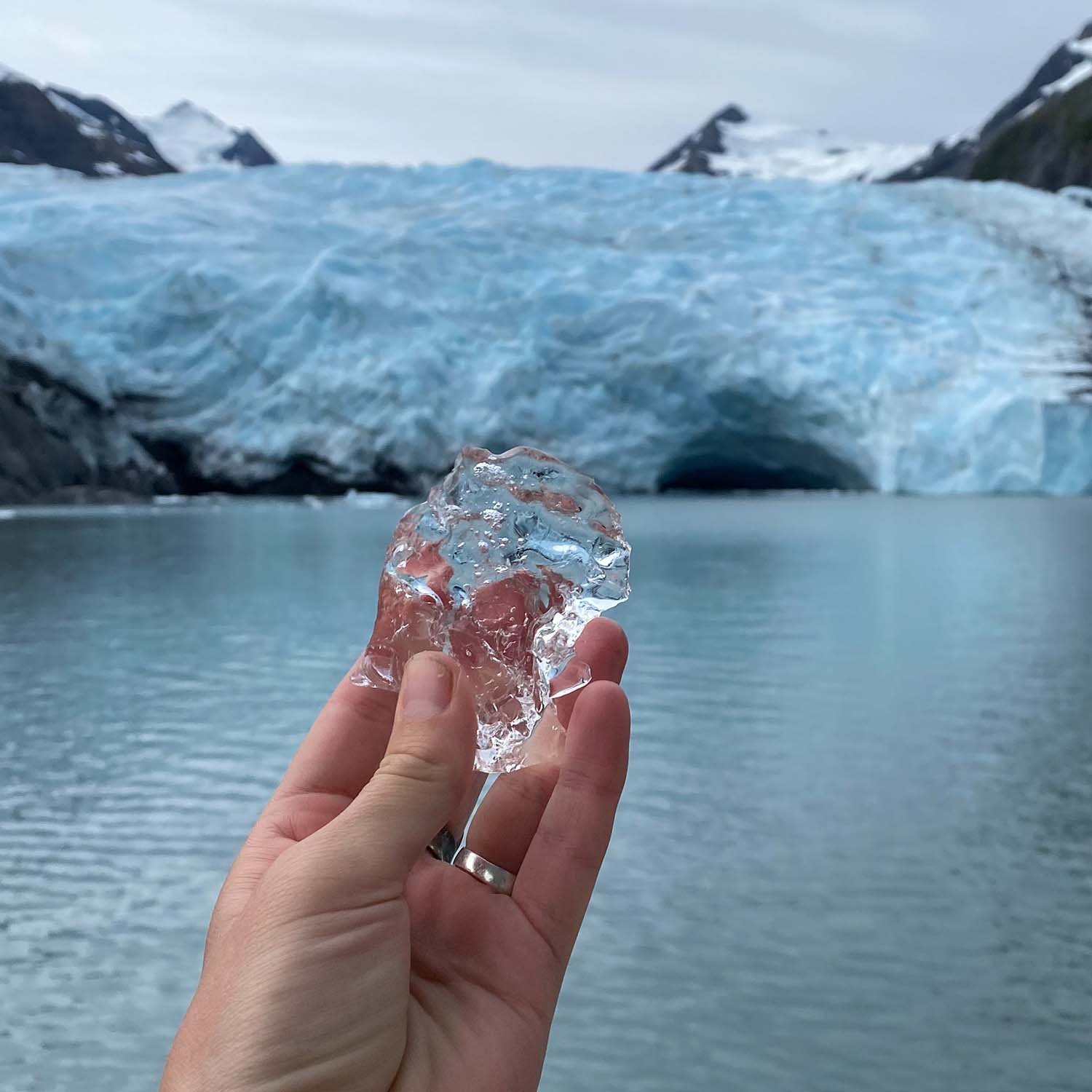 Person holding a piece of clear ice in front of a glacier and icy mountains.
