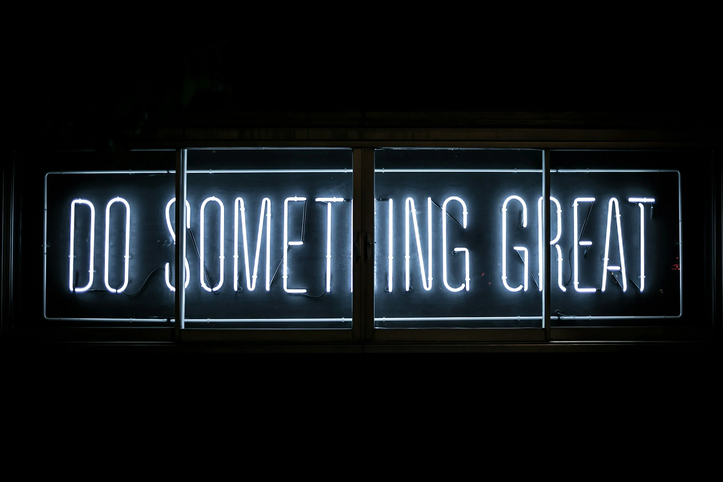 Neon sign reading 'DO SOMETHING GREAT' in white letters on a black background.