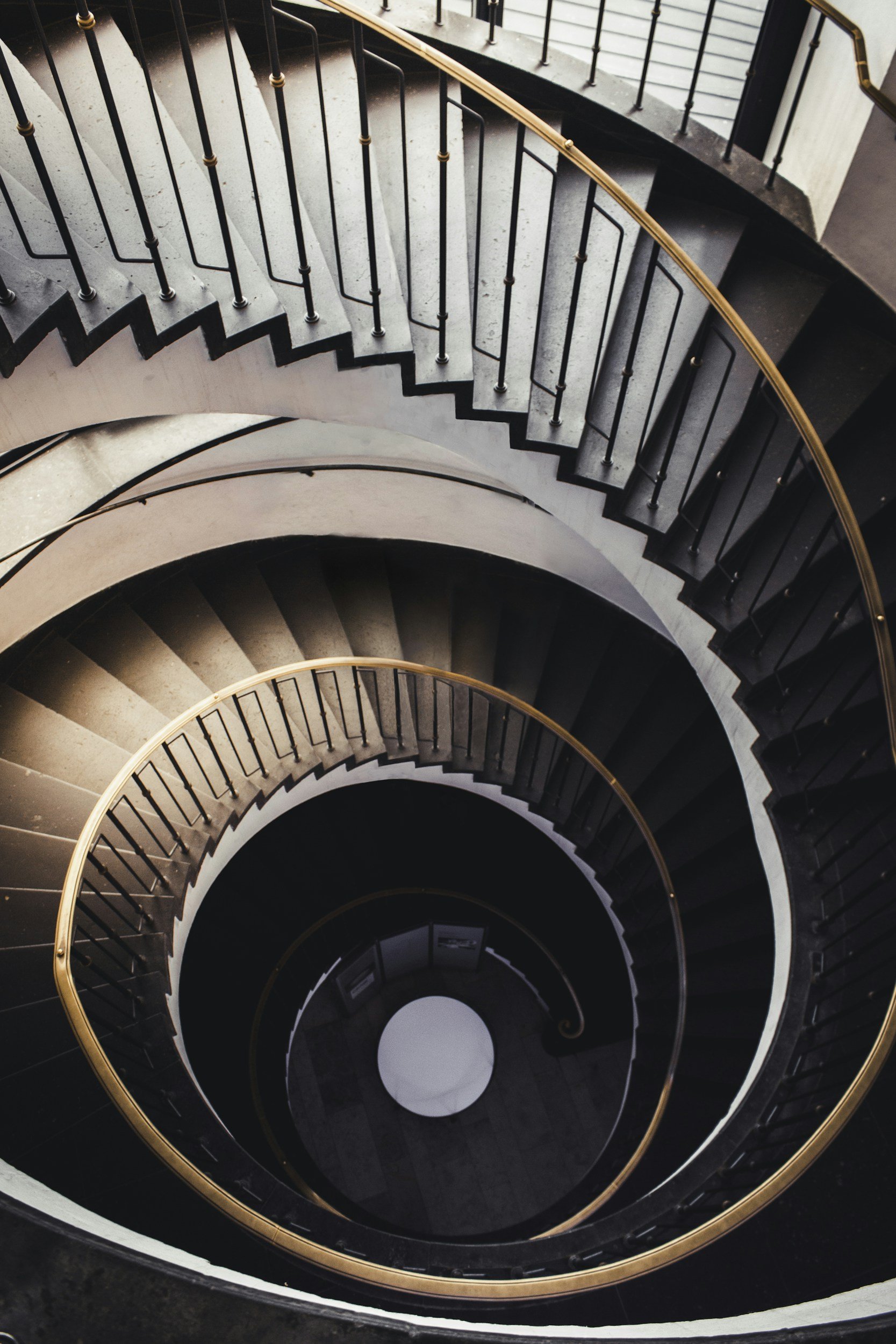 Top-down view of a spiral staircase with black steps, metal railings, and orange handrails, descending in a circular pattern.