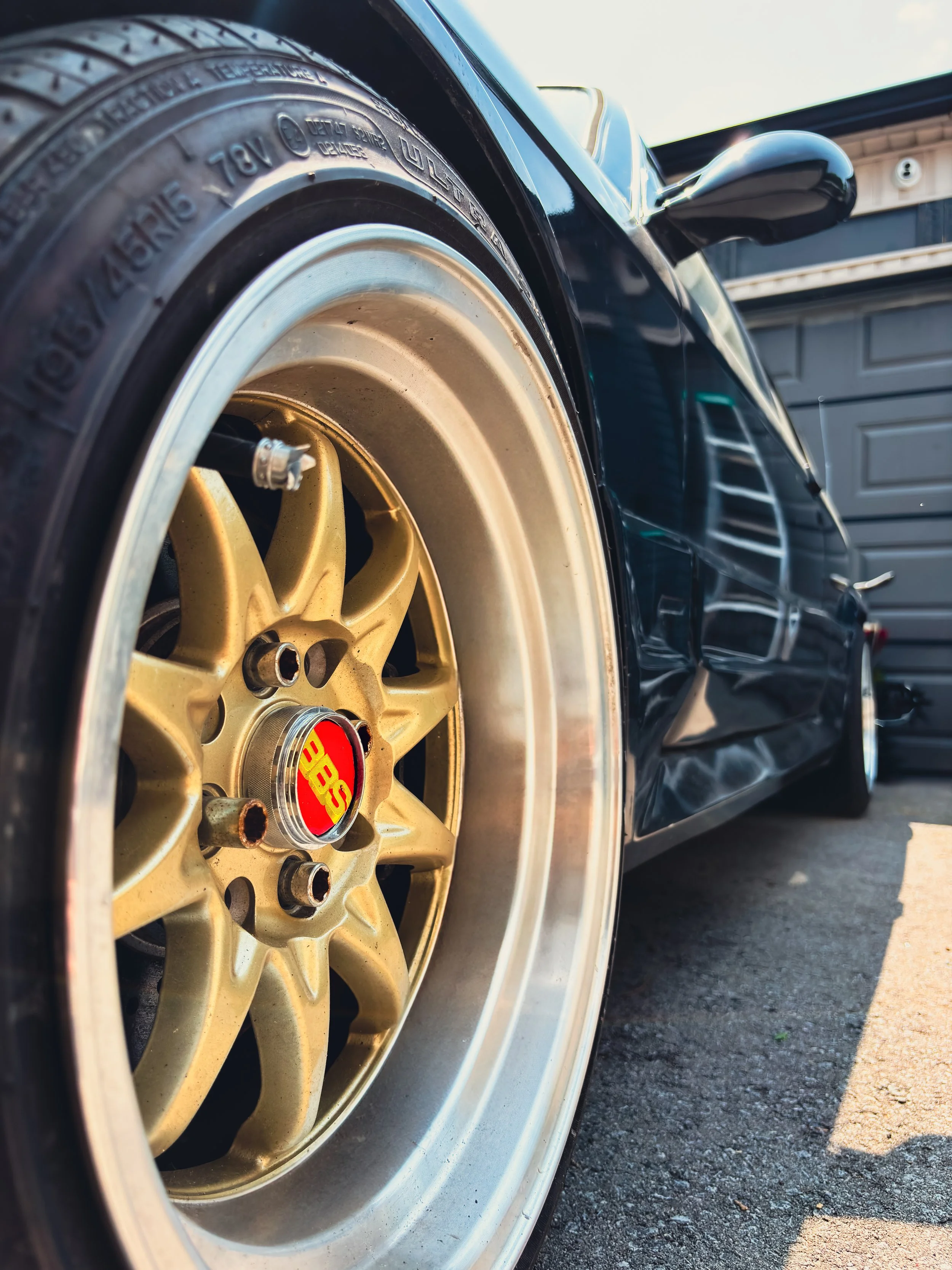 Close-up of a black sports car with gold wheels and low profile tires parked outside a garage.