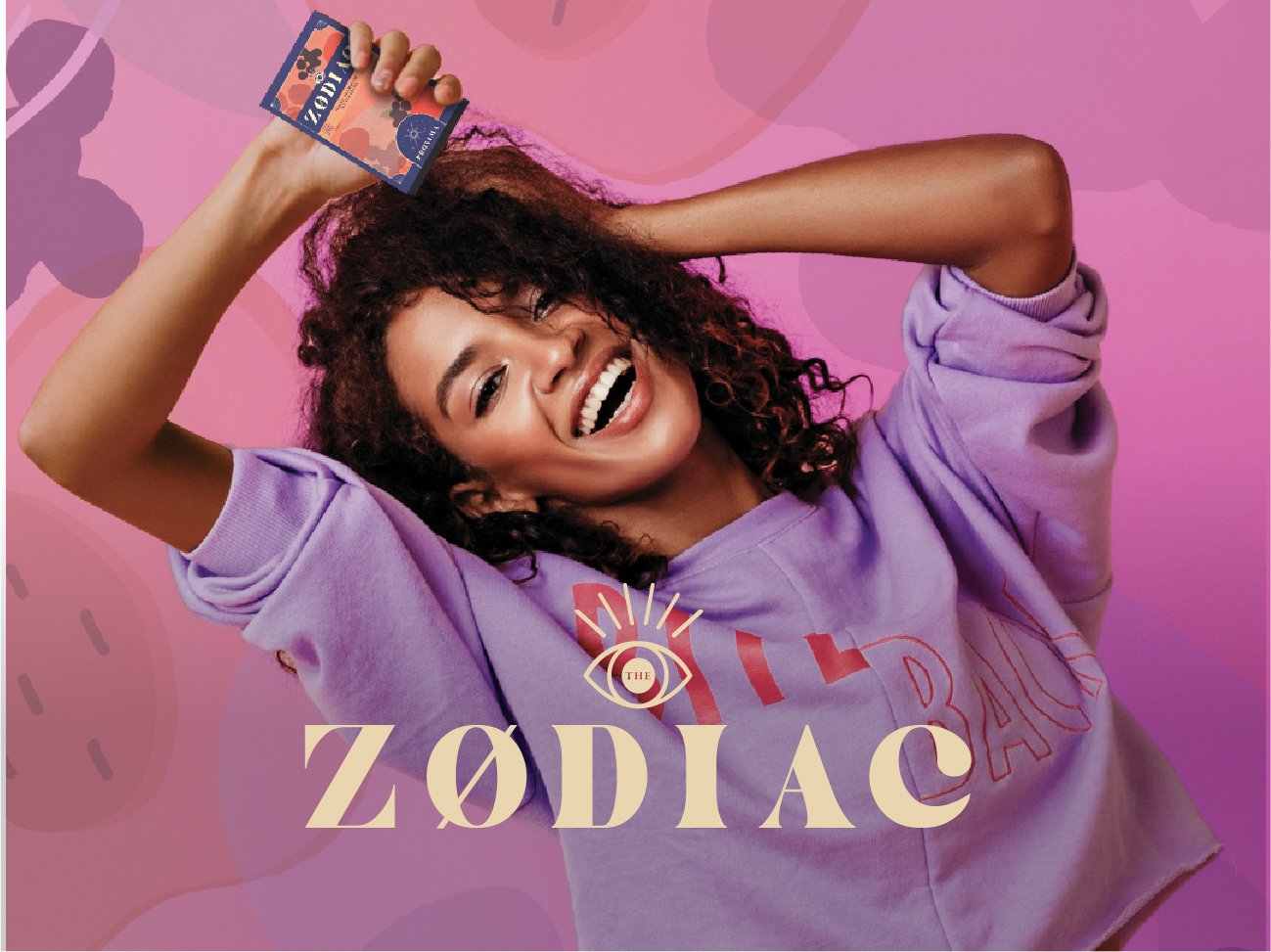 A woman smiling and holding a phone above her head, wearing a purple sweatshirt with the words "The Zodiac" on it, set against a pink and purple abstract background.