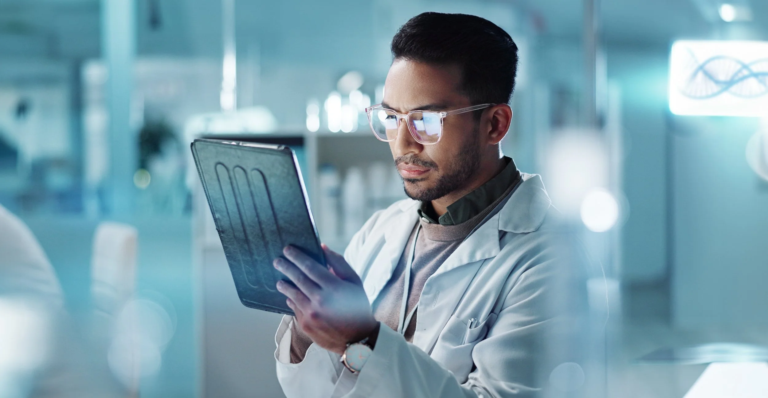 A male scientist in a white lab coat and glasses studying an X-ray image in a modern laboratory.