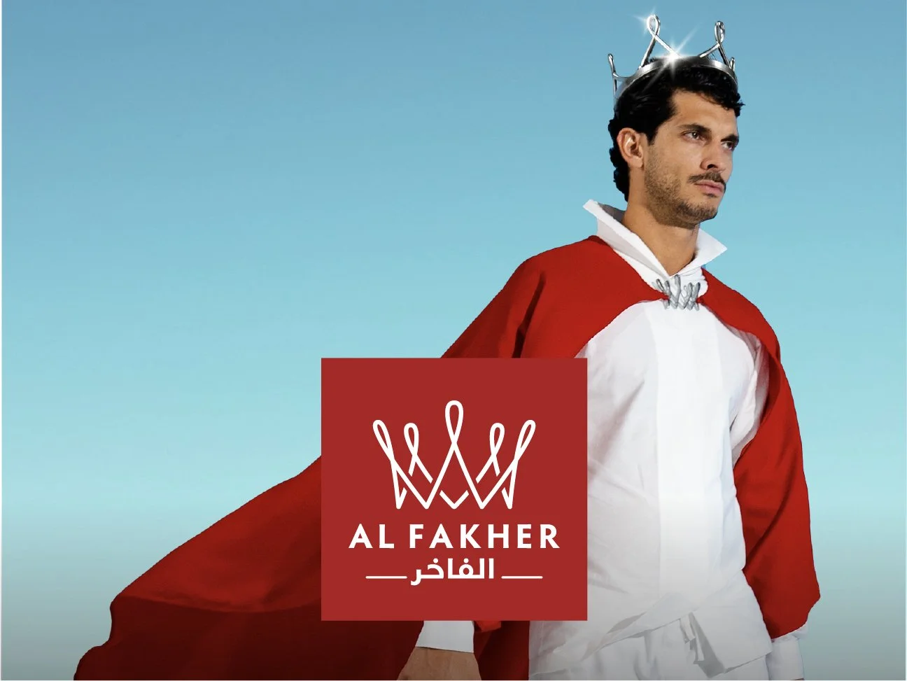 A man dressed as a king wearing a crown and a red cape over a white shirt, standing against a blue sky background, with a logo that reads "AL FAKHER" and Arabic text below.