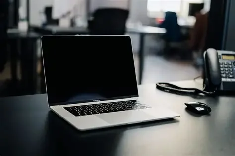 Open laptop on a desk in an office setting with a landline phone and mouse nearby.