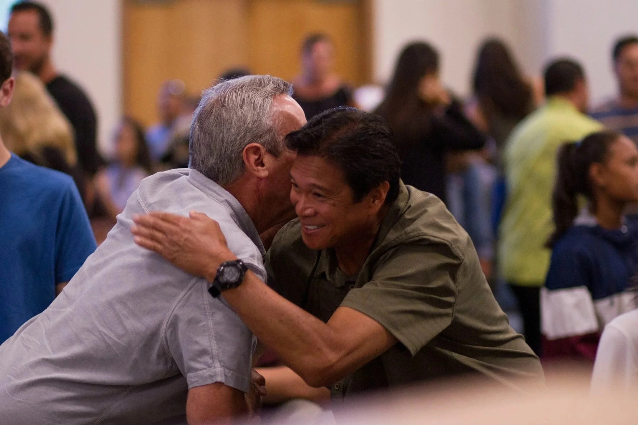 Two men sharing a warm embrace and smiling, surrounded by a crowd.