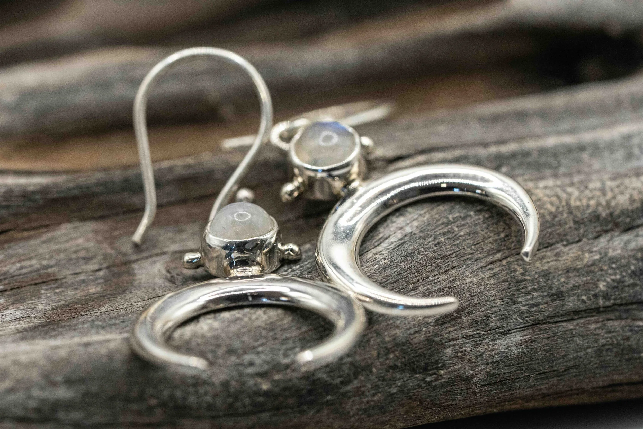 Close-up of silver hoop and crescent-shaped earrings with small beads, resting on weathered wooden surface.