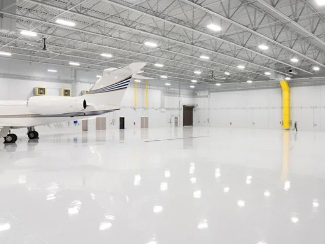Inside an airplane hangar with a small private jet on the left side and a person standing near the right wall.