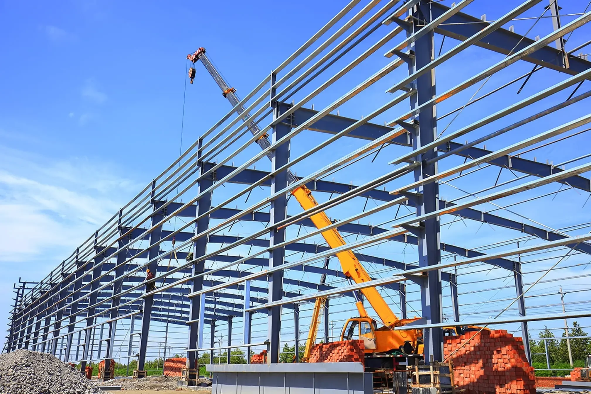 Construction of a steel framework building with a yellow crane lifting materials under a blue sky.
