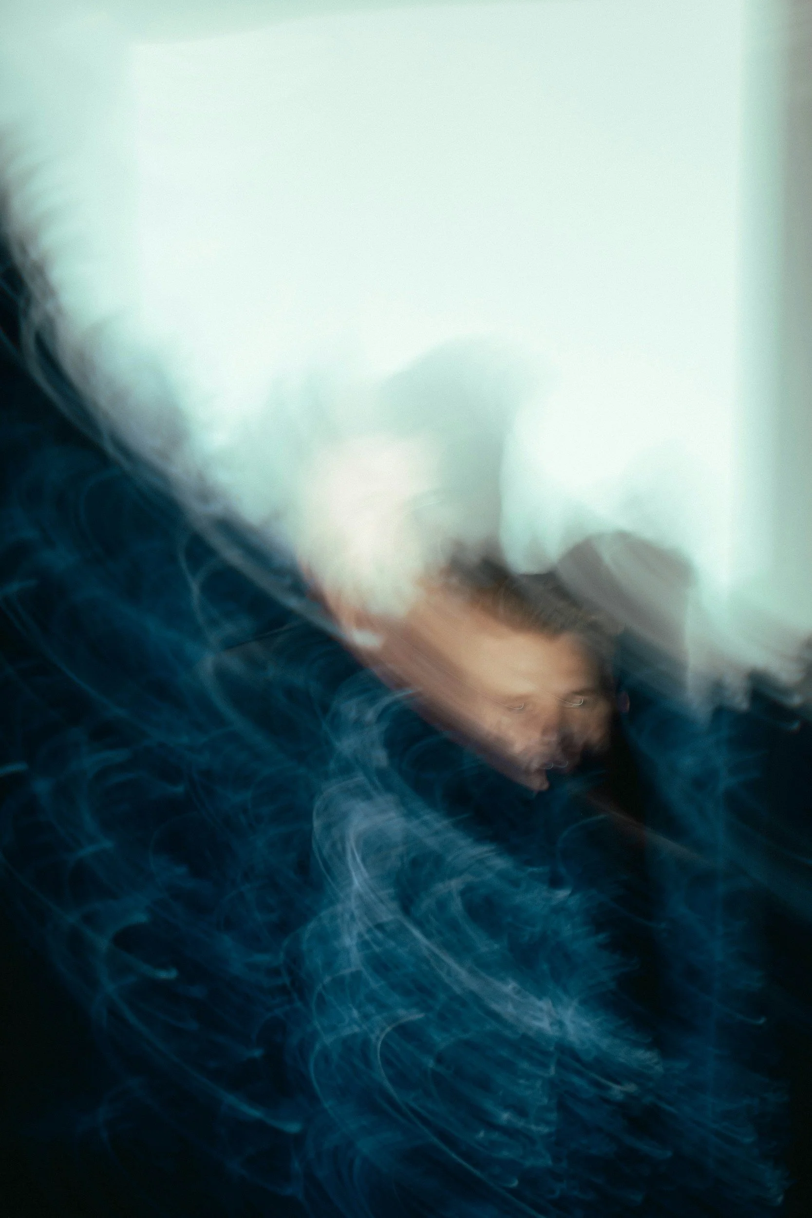 A person with brown hair and light skin, partially visible, surrounded by swirls of blue light in a dark environment, with abstract motion blur effects.