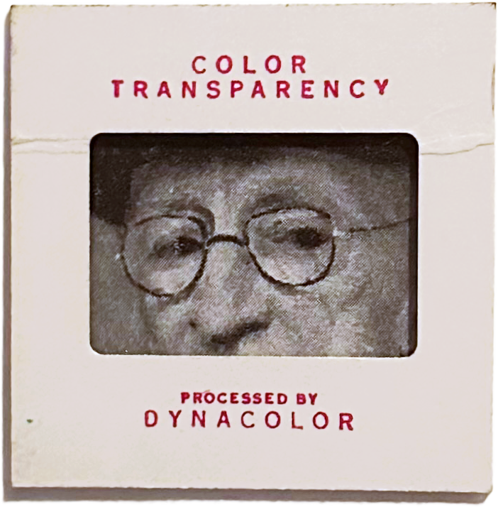 Black and white close-up portrait of a person wearing glasses, seen through a color transparency slide holder labeled 'Color Transparency, Processed by Dynacolor'.