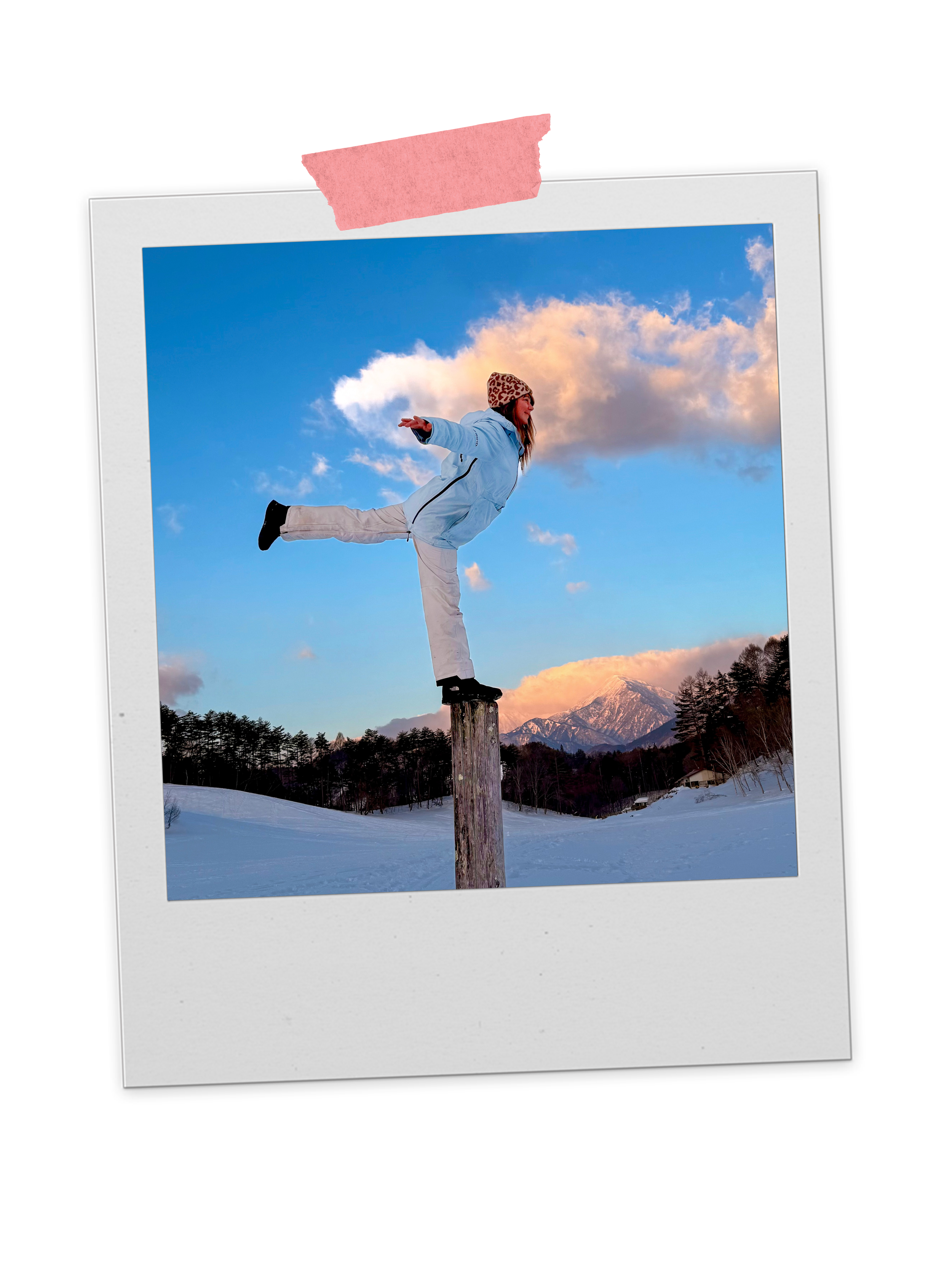 Woman balancing on a wooden post outdoors in a snowy landscape with mountains and trees, sky with clouds at sunset.