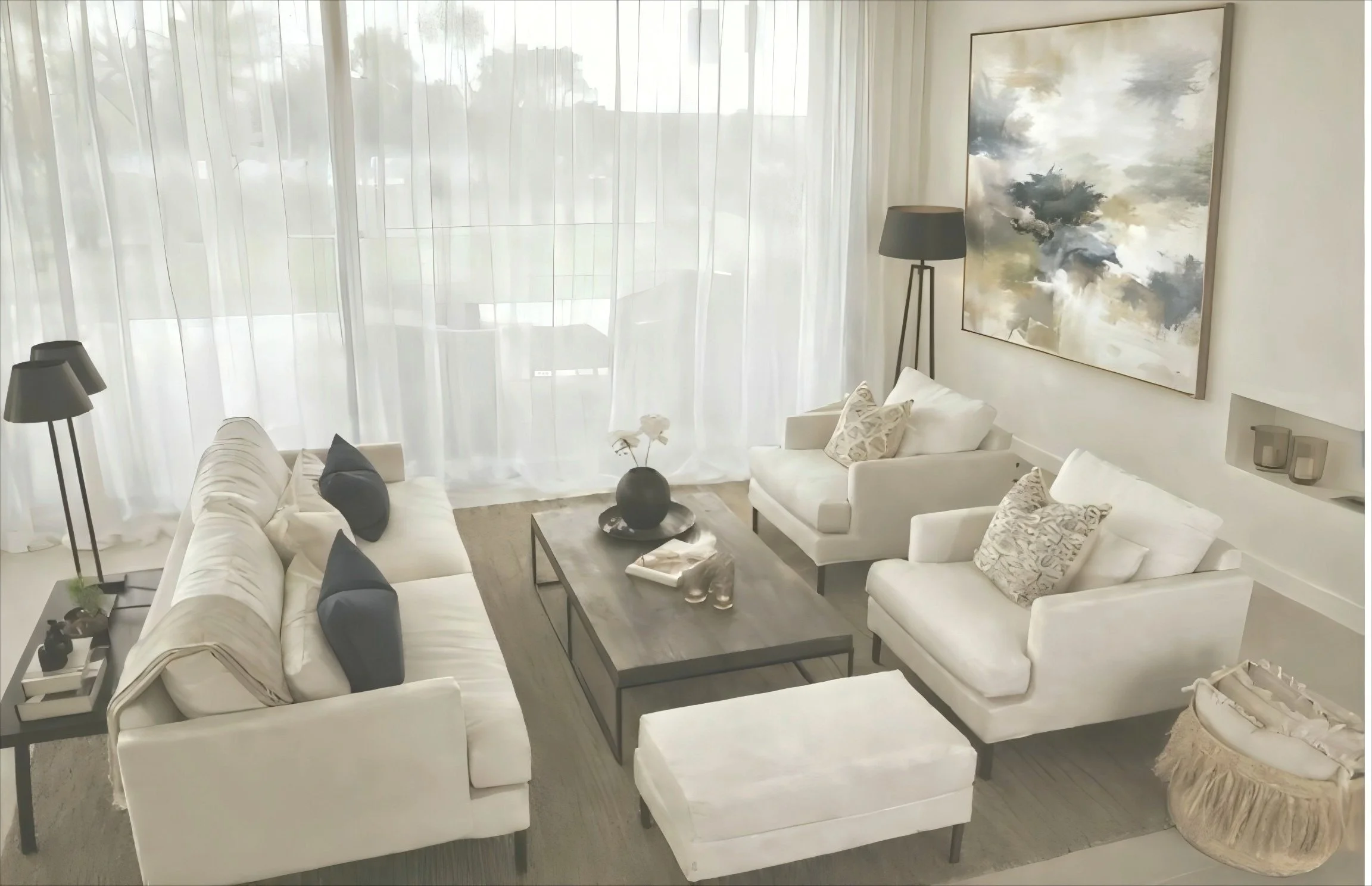 Bright living room with white walls and sheer curtains, furnished with white sofas, dark throw pillows, a wooden coffee table with decor, and abstract wall art.