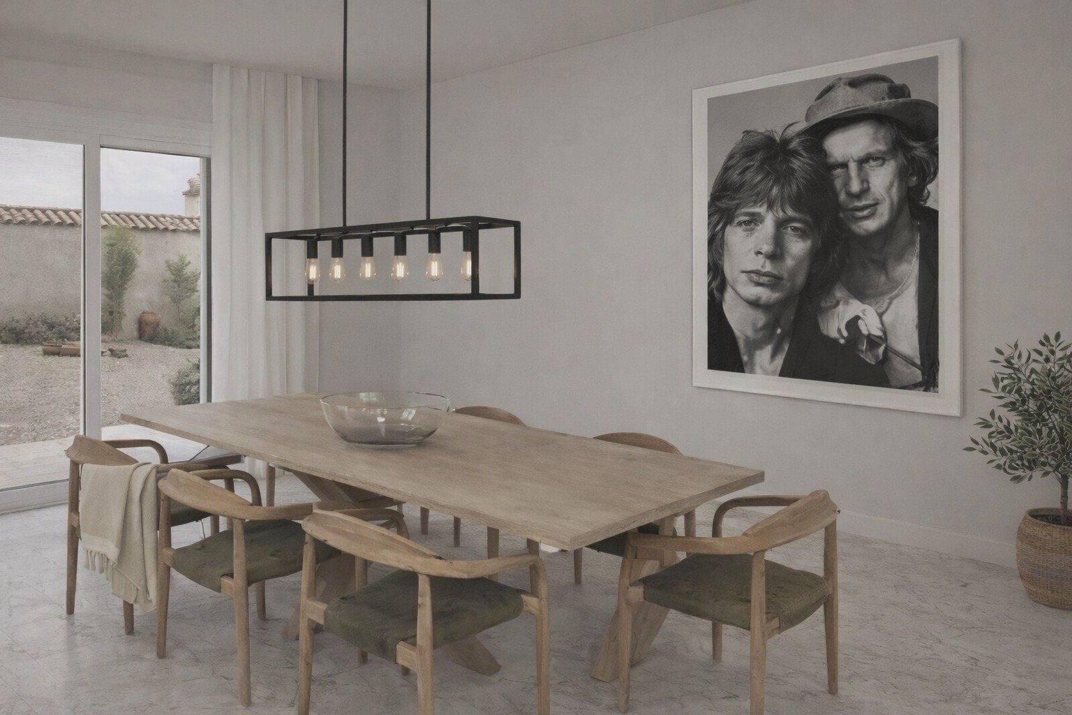 A modern dining room with a wooden table and six chairs, a large black pendant light fixture, a large black-and-white portrait of two people on the wall, a potted plant in the corner, and sliding glass doors leading outside.