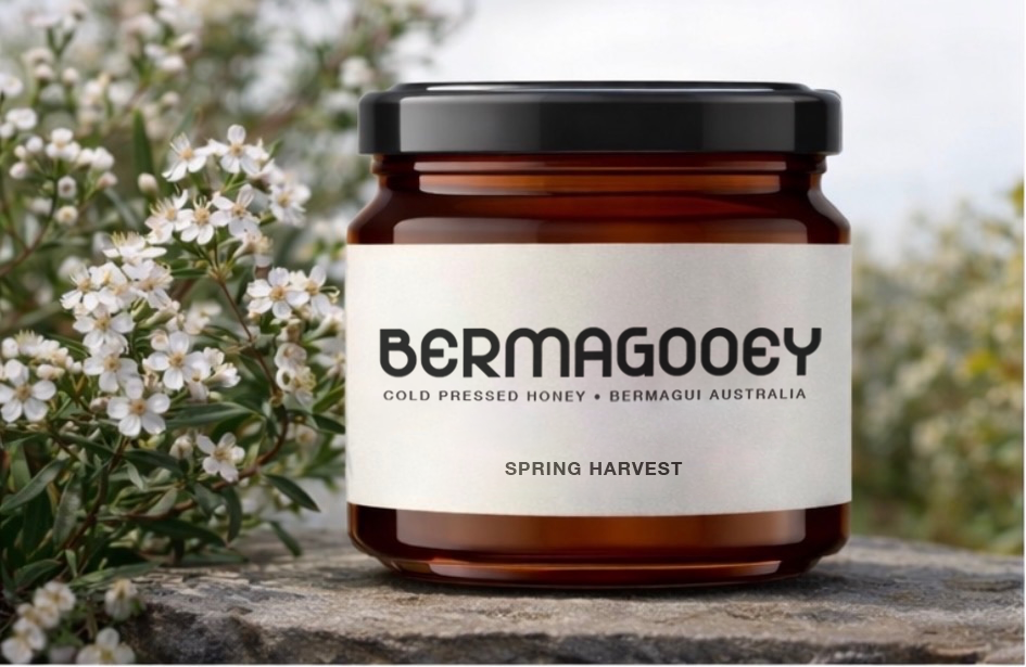 A jar of Bermagouy spring harvest honey placed on a stone surface with white flowering plants in the background.