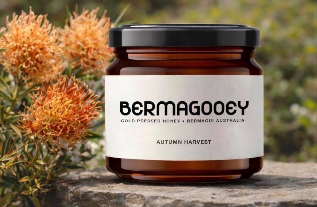 A jar of Bermagooey Autumn Harvest honey placed on a stone surface with orange and yellow flowers in the background.