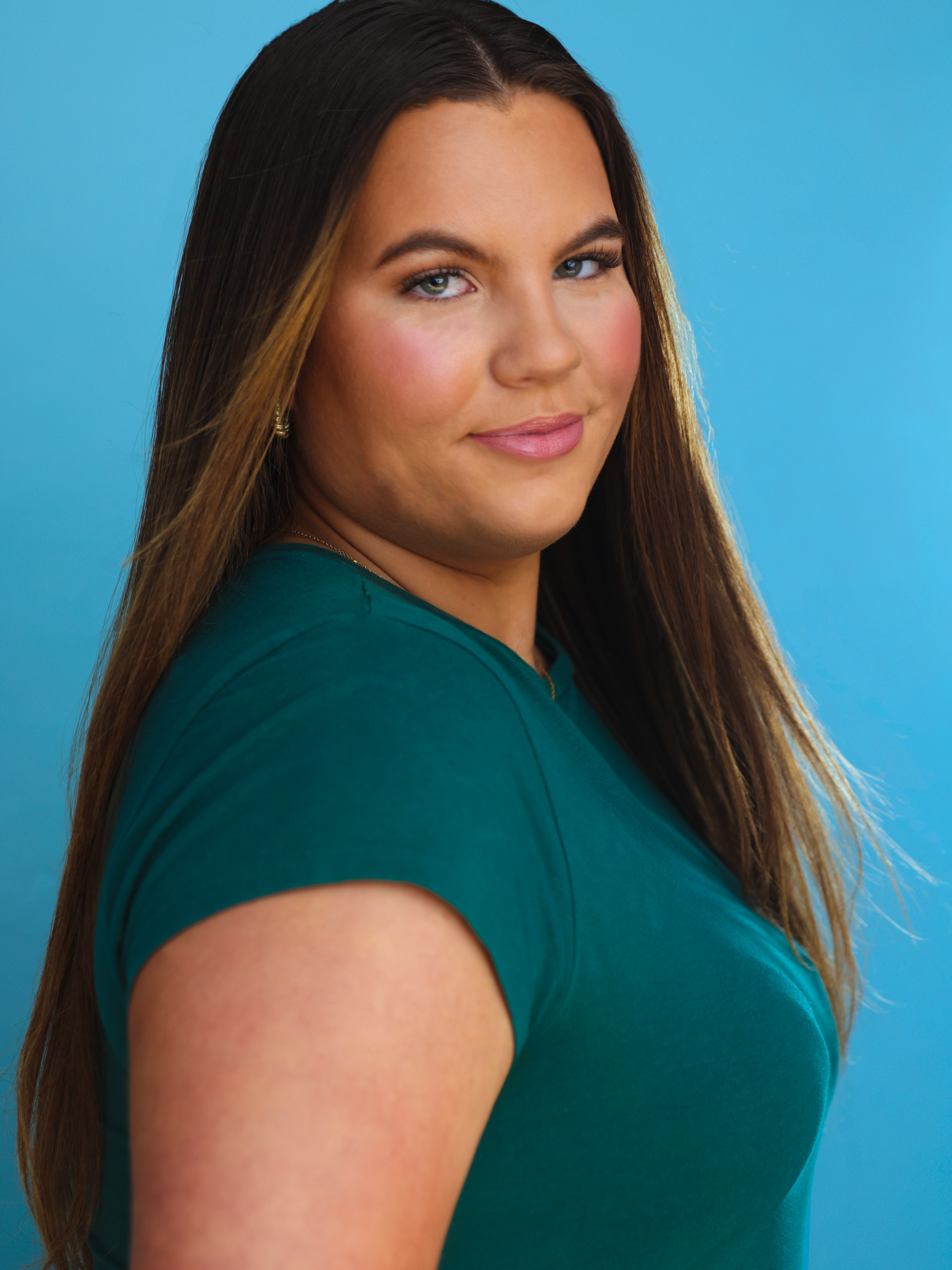 A young woman with long brown hair and blue eyes posing against a blue background.
