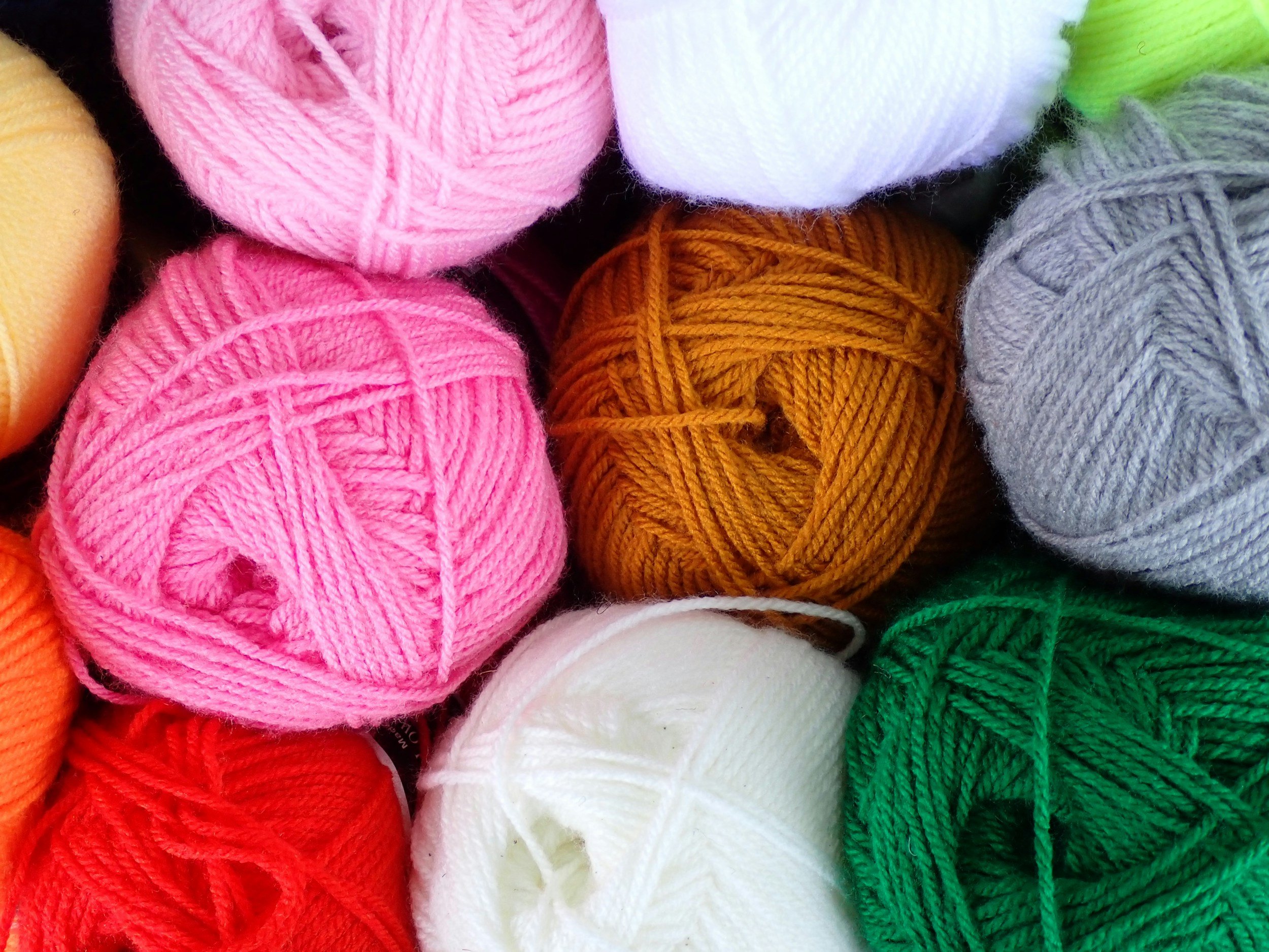 Close-up of colorful balls of yarn in pink, orange, yellow, white, green, gray, and purple.