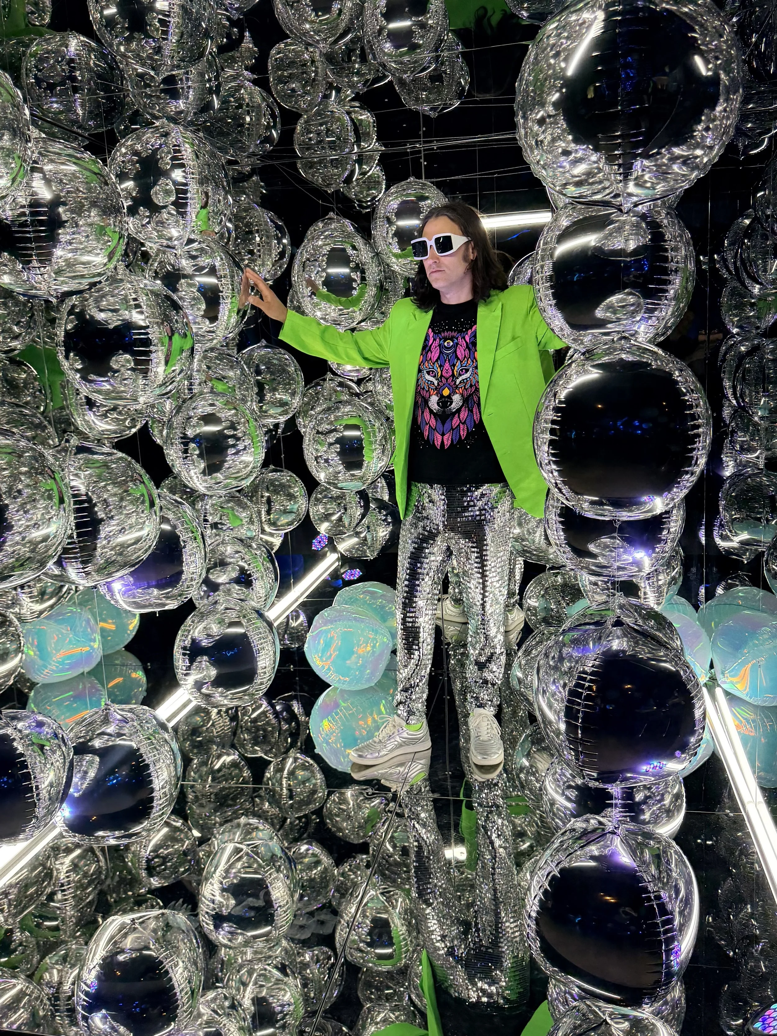 Band singer in a vibrant green suit jacket and disco pants inside the mirror cube photo booth