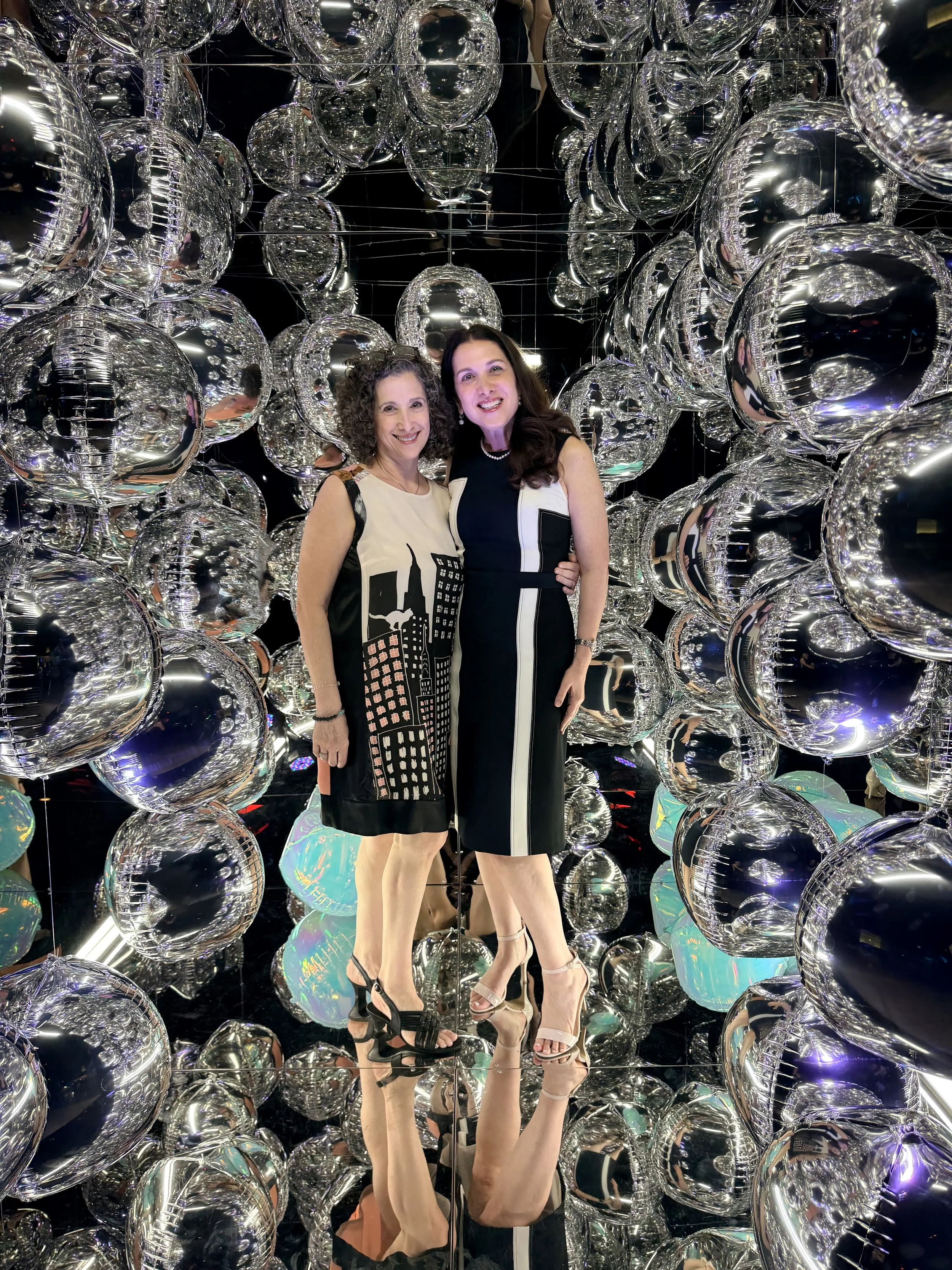 two women smiling at a bar mitzvah and looking at the camera  inside the mirror photo cube booth