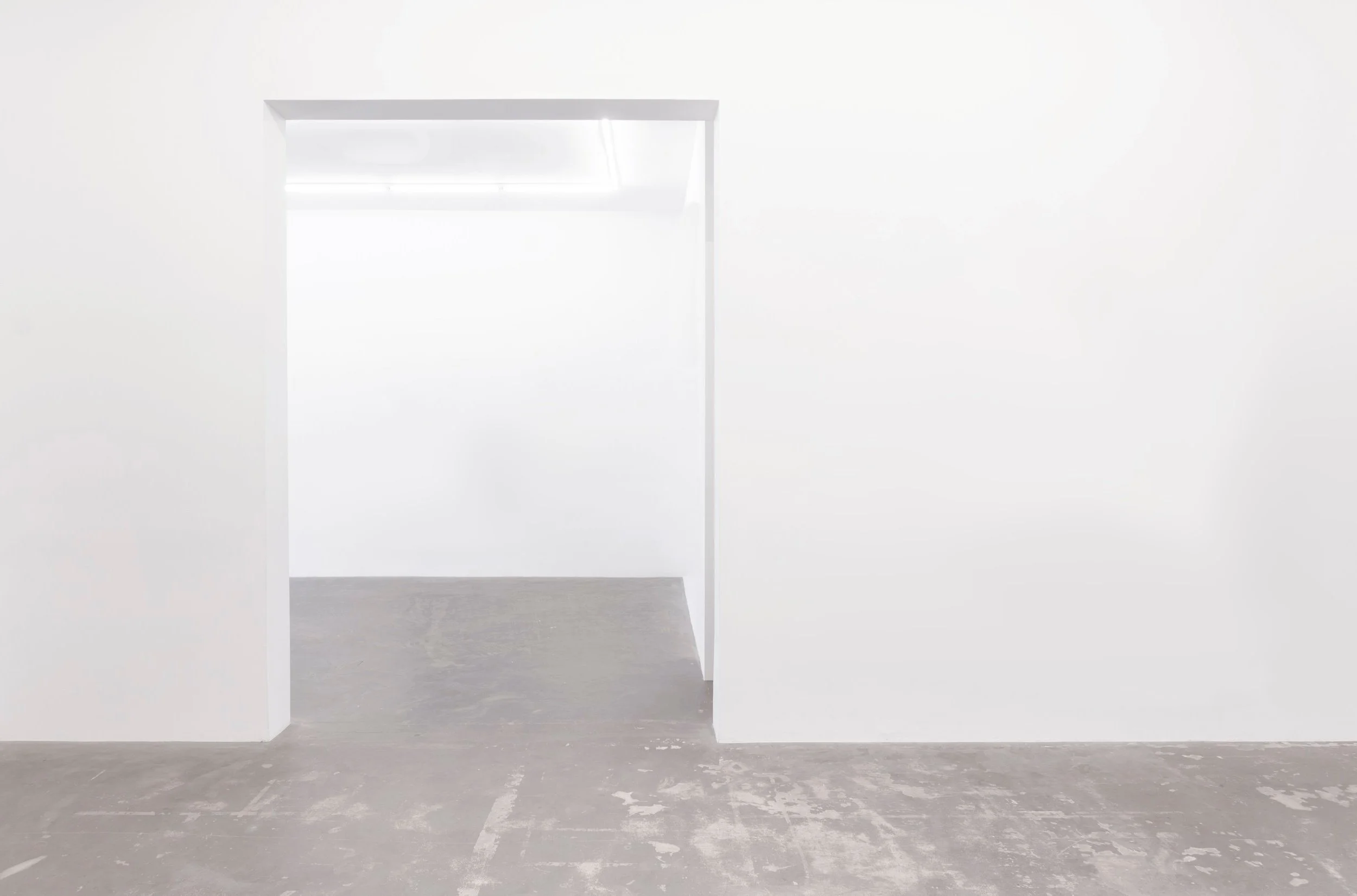 White interior space with an open doorway leading to a bright room, concrete floor, minimalistic setting.