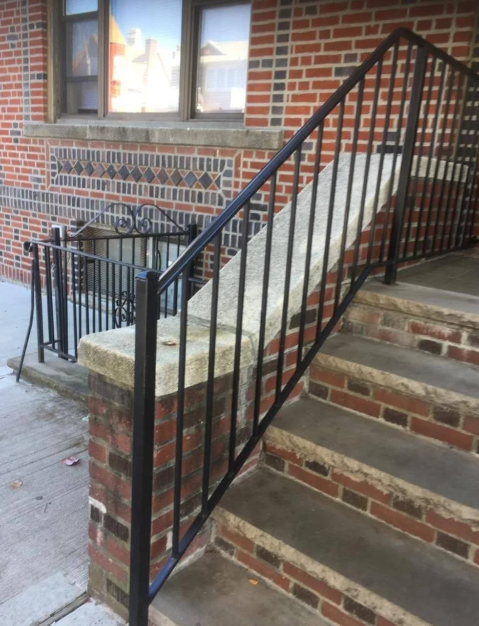 Concrete staircase with black metal railing leading to a building entrance, brick exterior wall with decorative brickwork, and a window above.