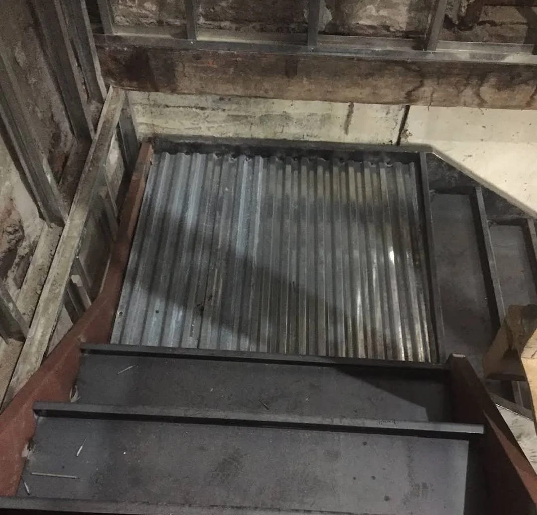 A metal staircase in an unfinished building under construction, with wooden framing and exposed brick walls.
