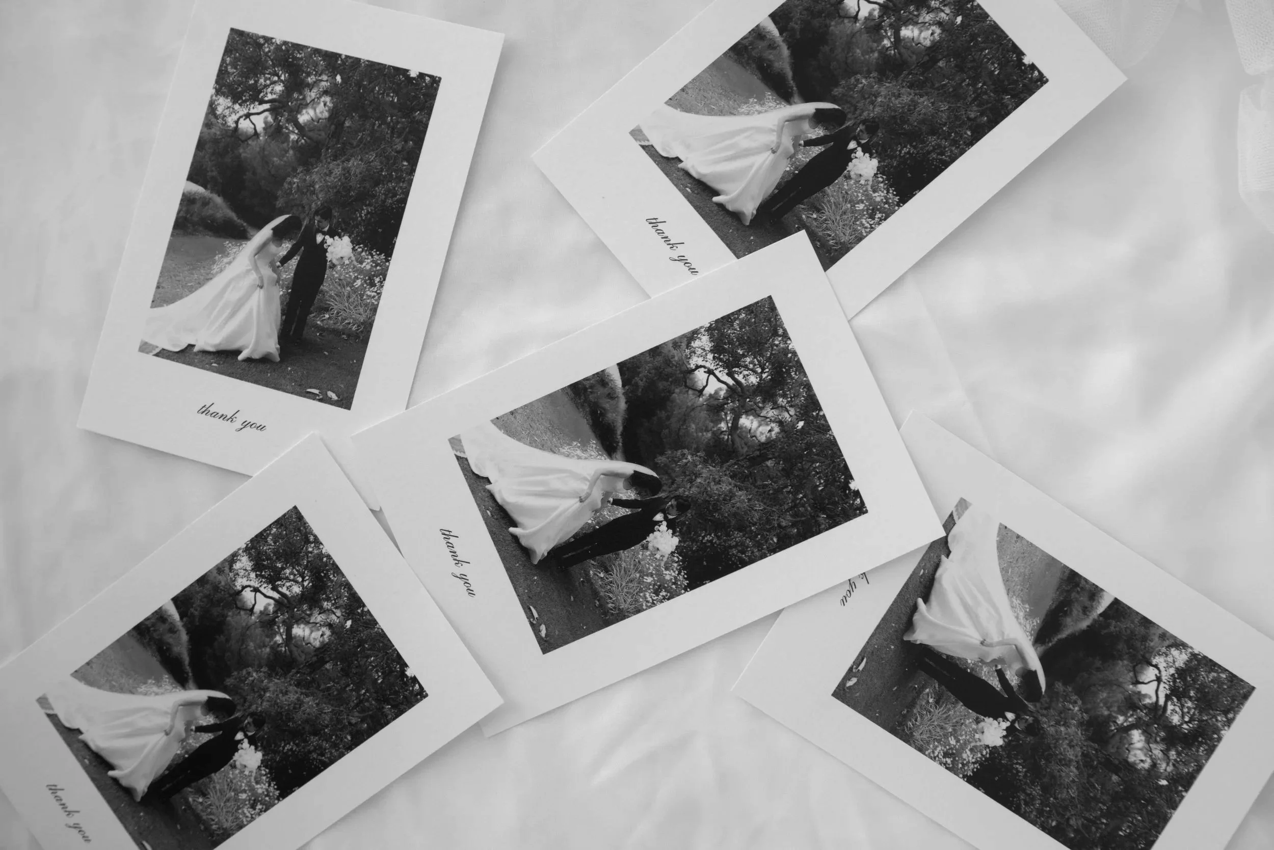 Multiple black-and-white printed photographs of a bride and groom on a wedding day, with several couple photos outdoors, some with trees in the background, and a message that says 'thank you' at the bottom.