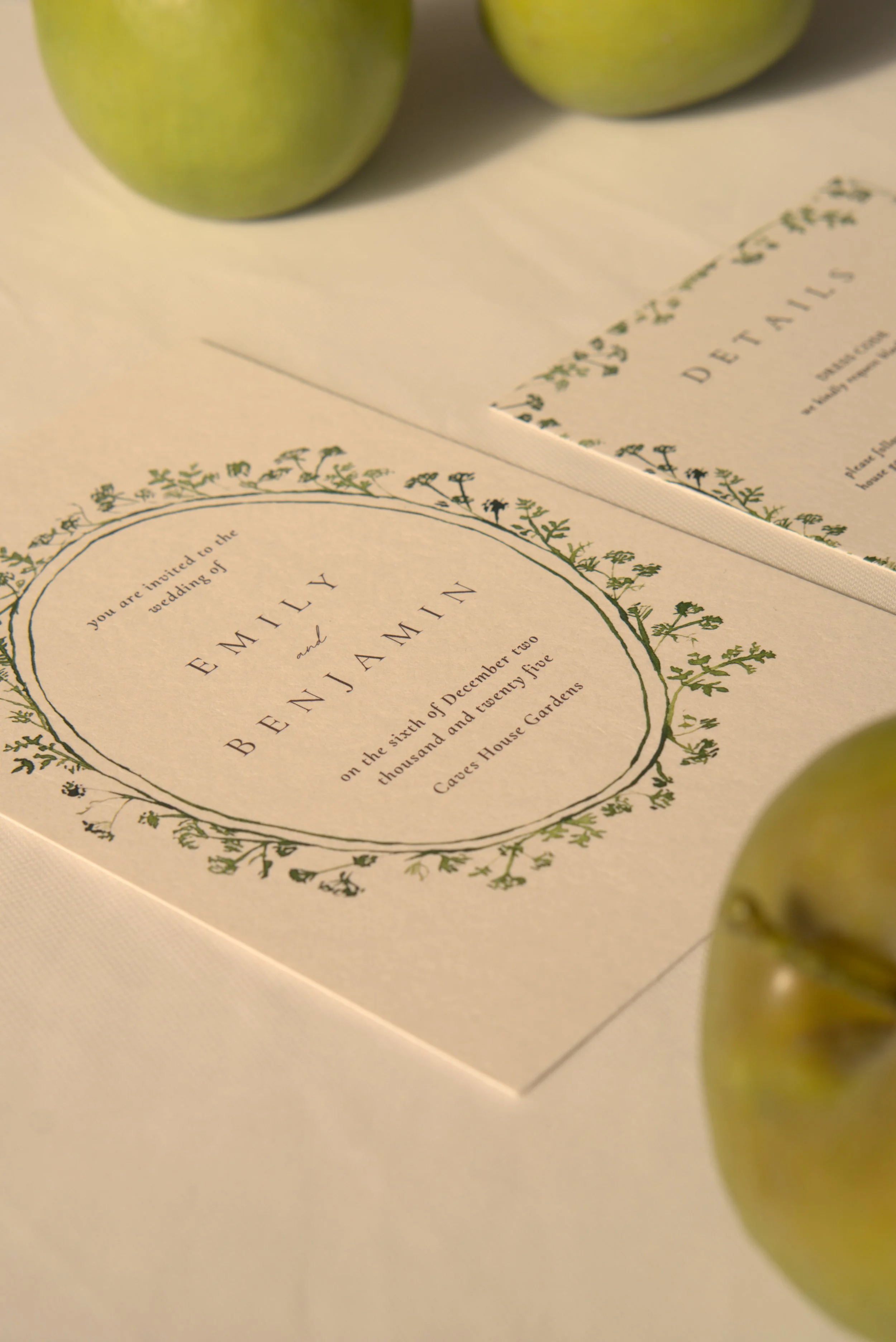 Wedding invitation with green decorative border and two green apples nearby.