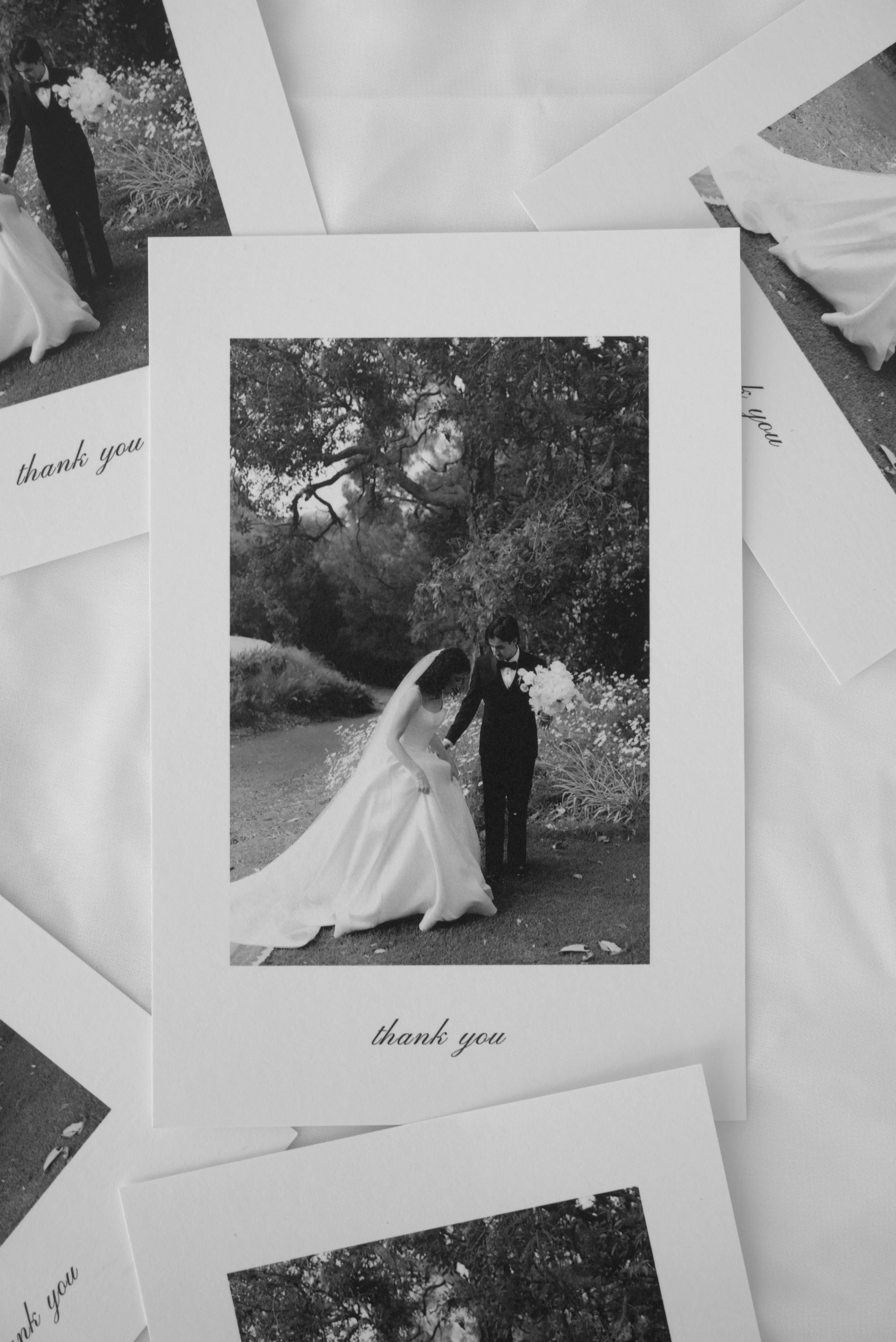 Black and white photo of a bride and groom holding hands outdoors in front of trees, with a "thank you" message at the bottom.