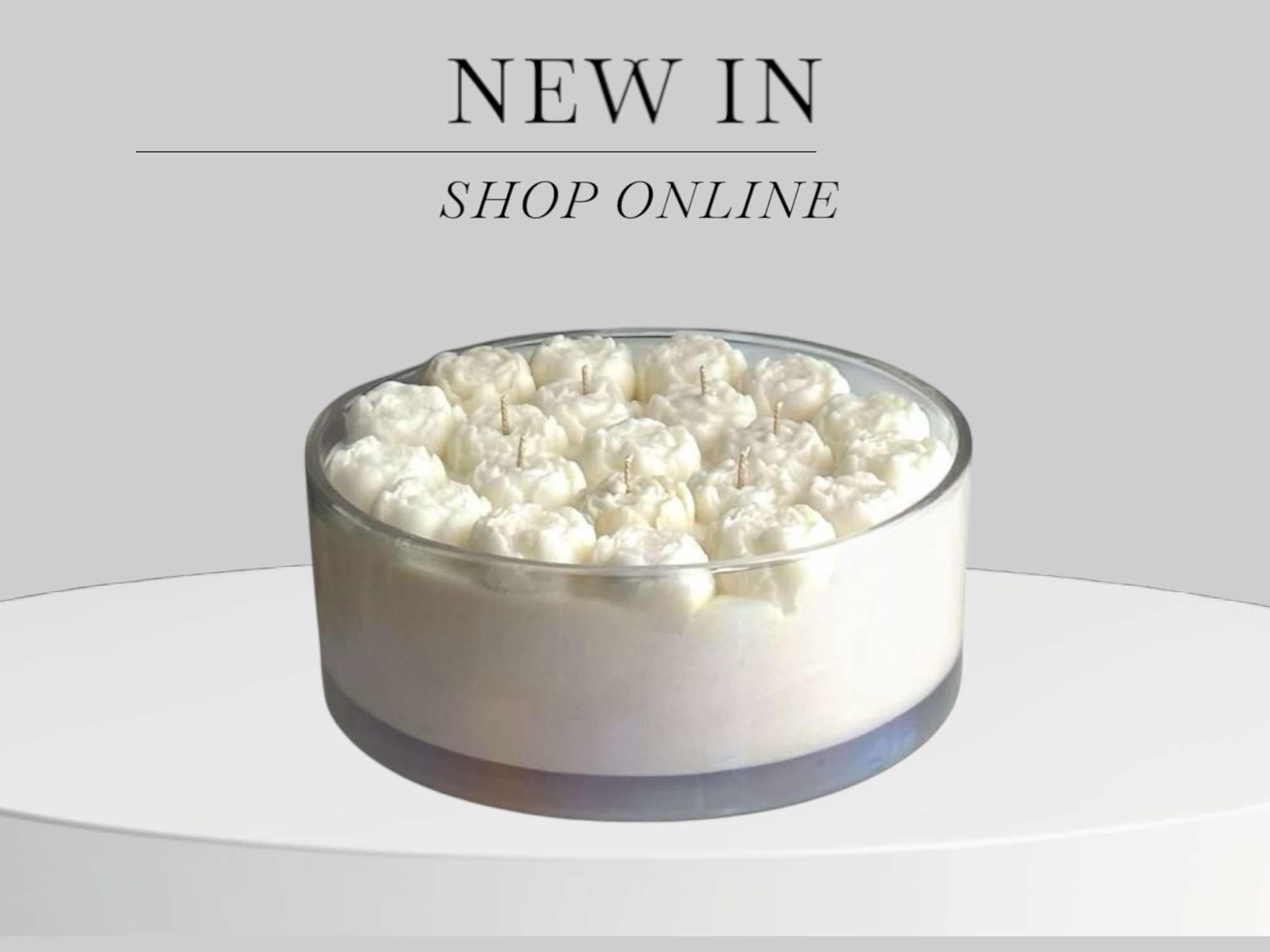 A round glass container filled with white dessert topped with small candles, with text above saying 'New In' and 'Shop Online' on a light gray background.