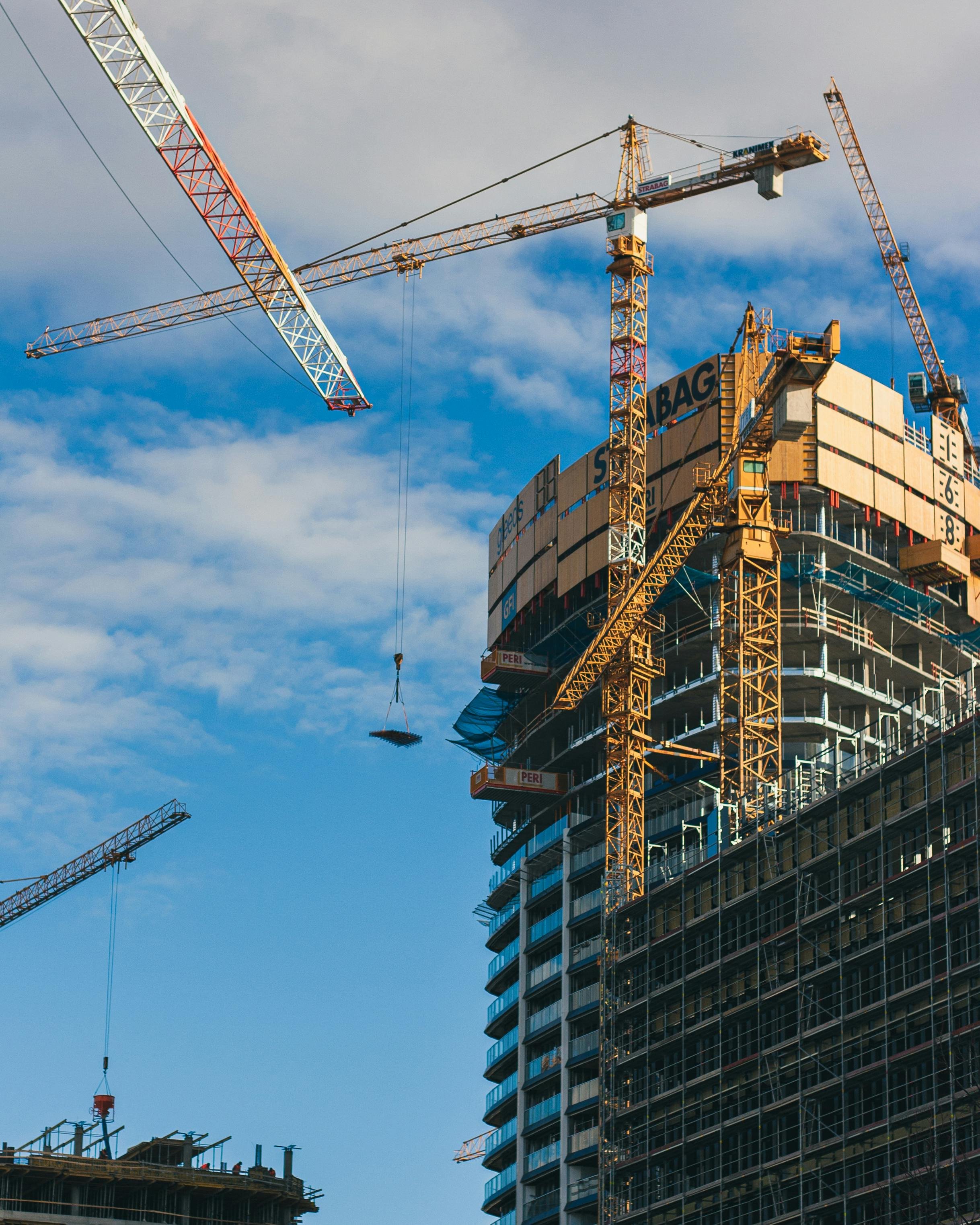 Construction site with multiple cranes building a high-rise building under a partly cloudy sky.