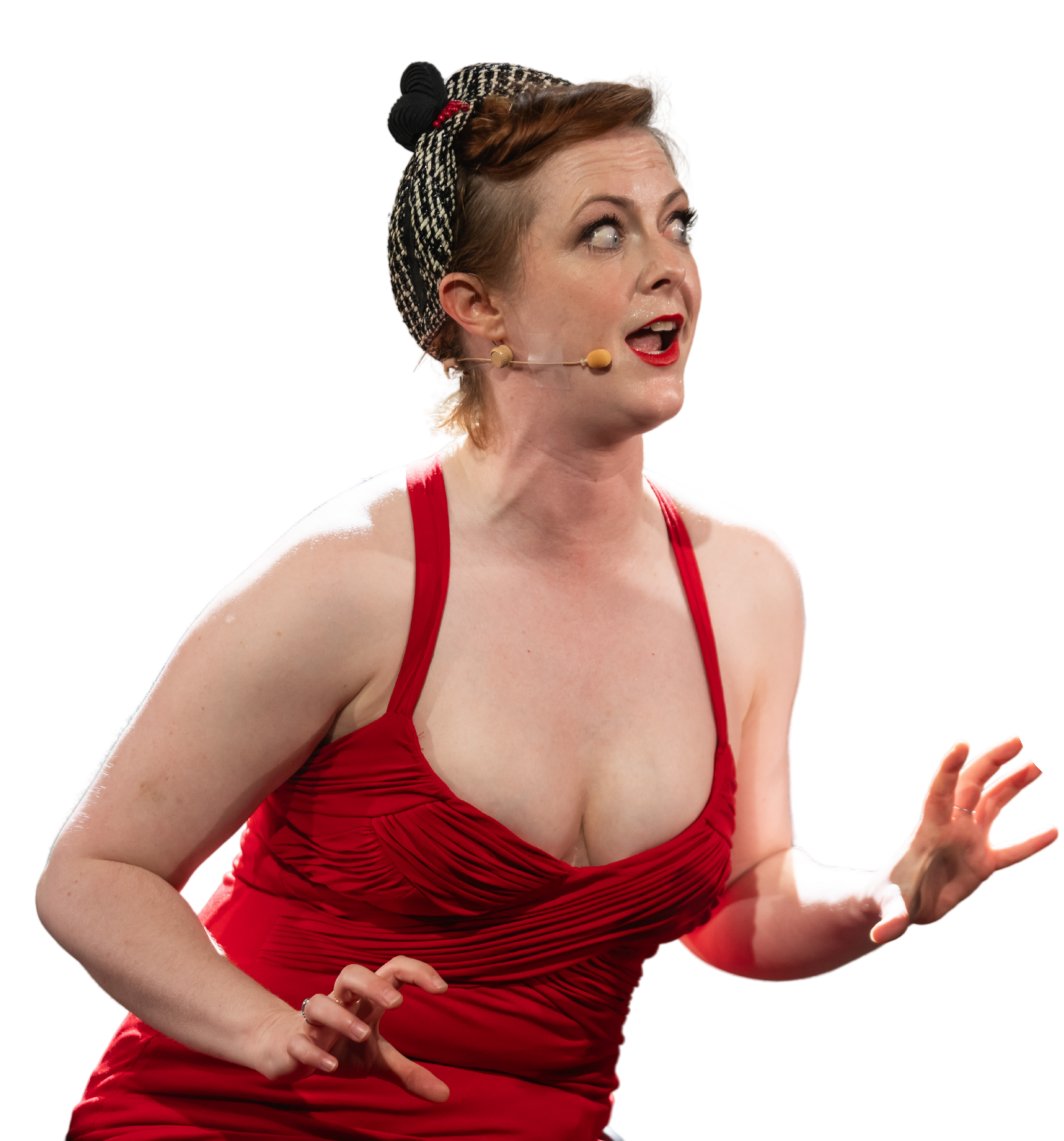 A woman with short red hair, wearing a red dress and a black and white headscarf, speaking into a microphone headset with a surprised or expressive facial expression, against a plain background.