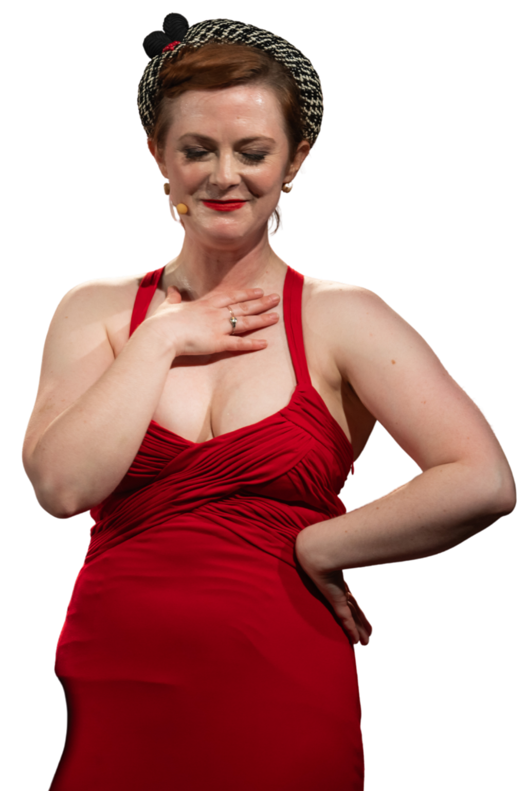 A woman with short red hair, wearing a red dress with spaghetti straps, standing with her eyes closed and one hand on her chest, the other on her hip, against a black background.