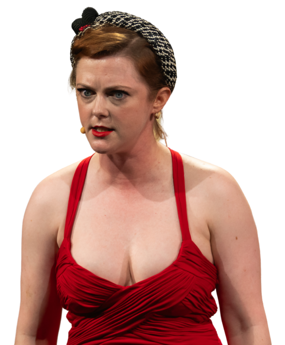 A woman with short red hair wearing a black and white headscarf and a red dress, speaking passionately with an intense facial expression.