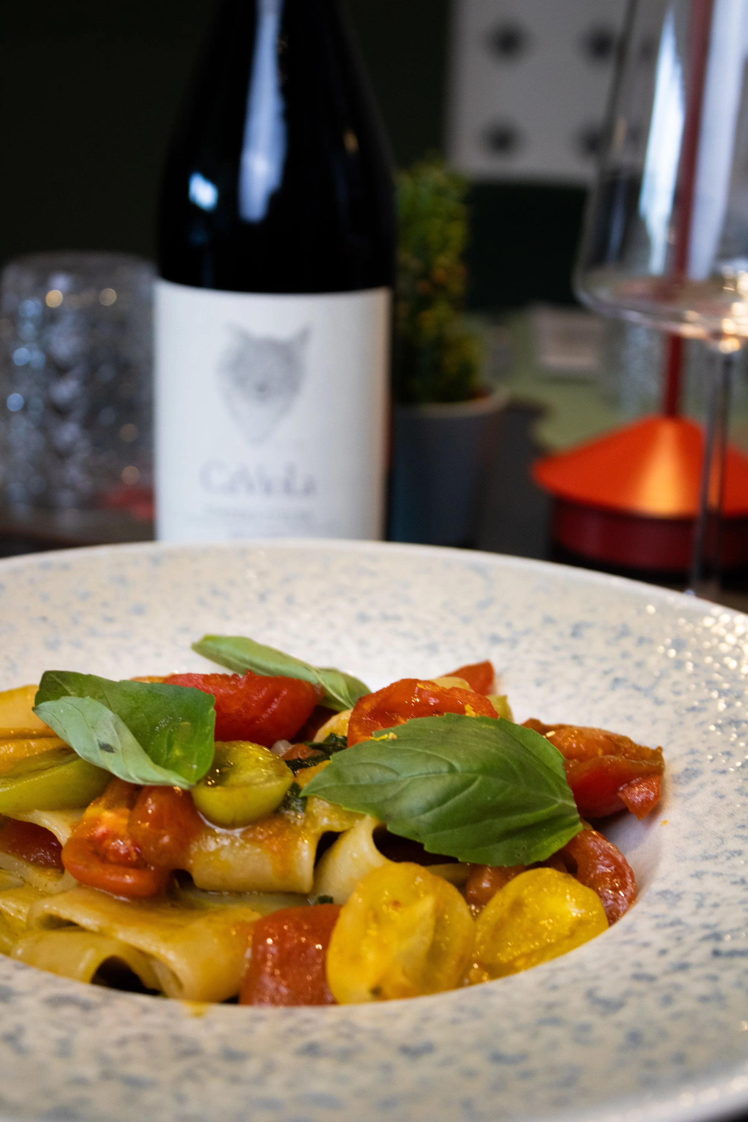 Primo piano di un piatto di pasta con pomodorini, foglie di basilico fresco e zucchine gialle.