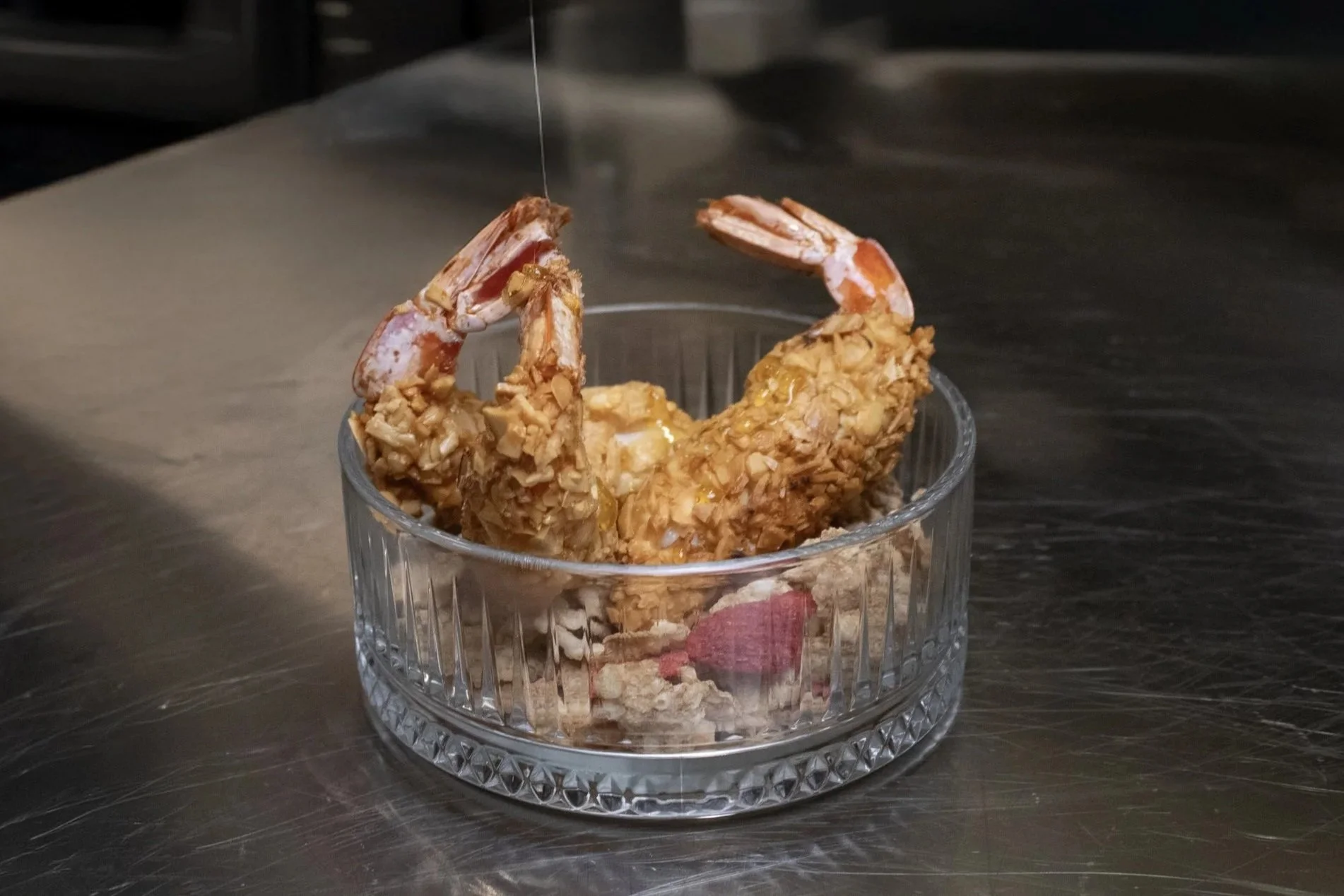 Deep-fried shrimp in a clear glass bowl on a stainless steel surface.