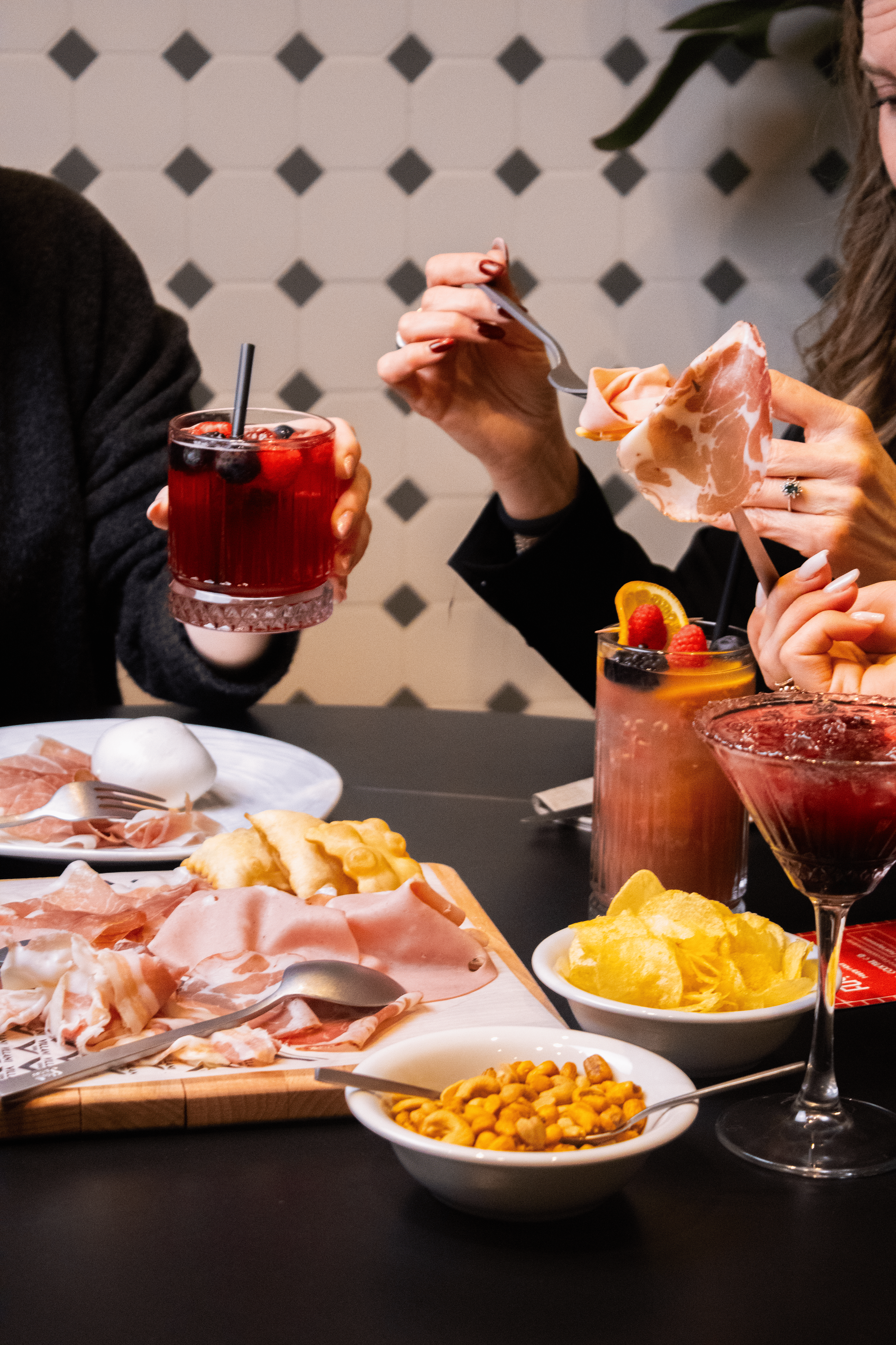 People enjoying a meal with charcuterie, chips, and colorful drinks at a restaurant.